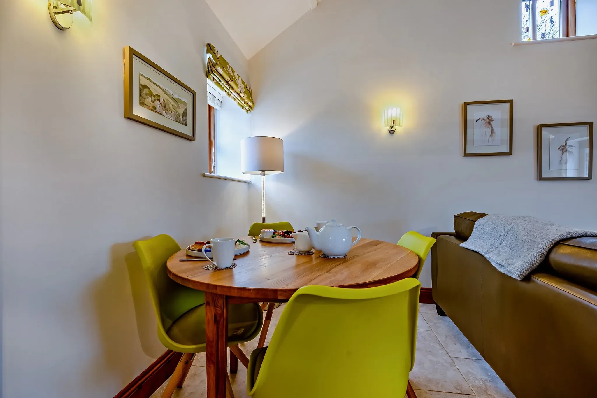Barley Park dining corner with a round oak table, lime-green chairs and a tea set laid out beneath a tall vaulted ceiling.