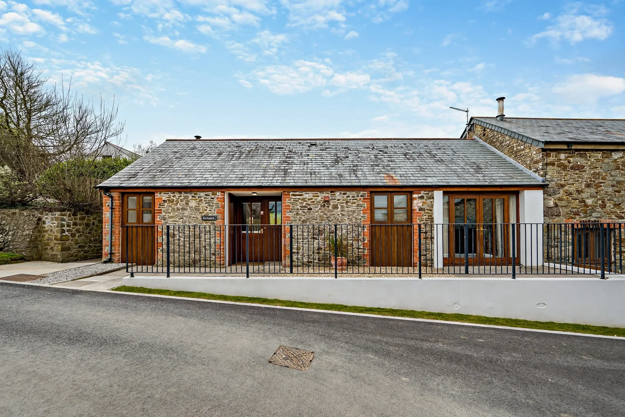 Barley Park full front elevation showing the converted stone barn with oak-framed doors and windows and a small lawned terrace.