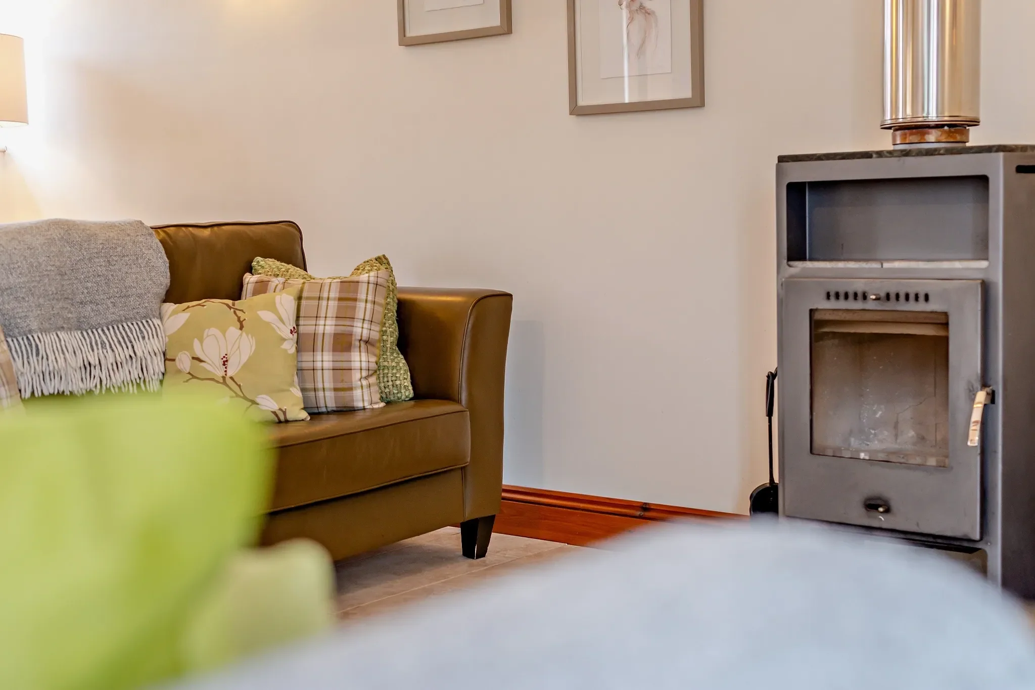 Barley Park sitting area close-up of a leather armchair with floral cushions beside the lit wood-burning stove.