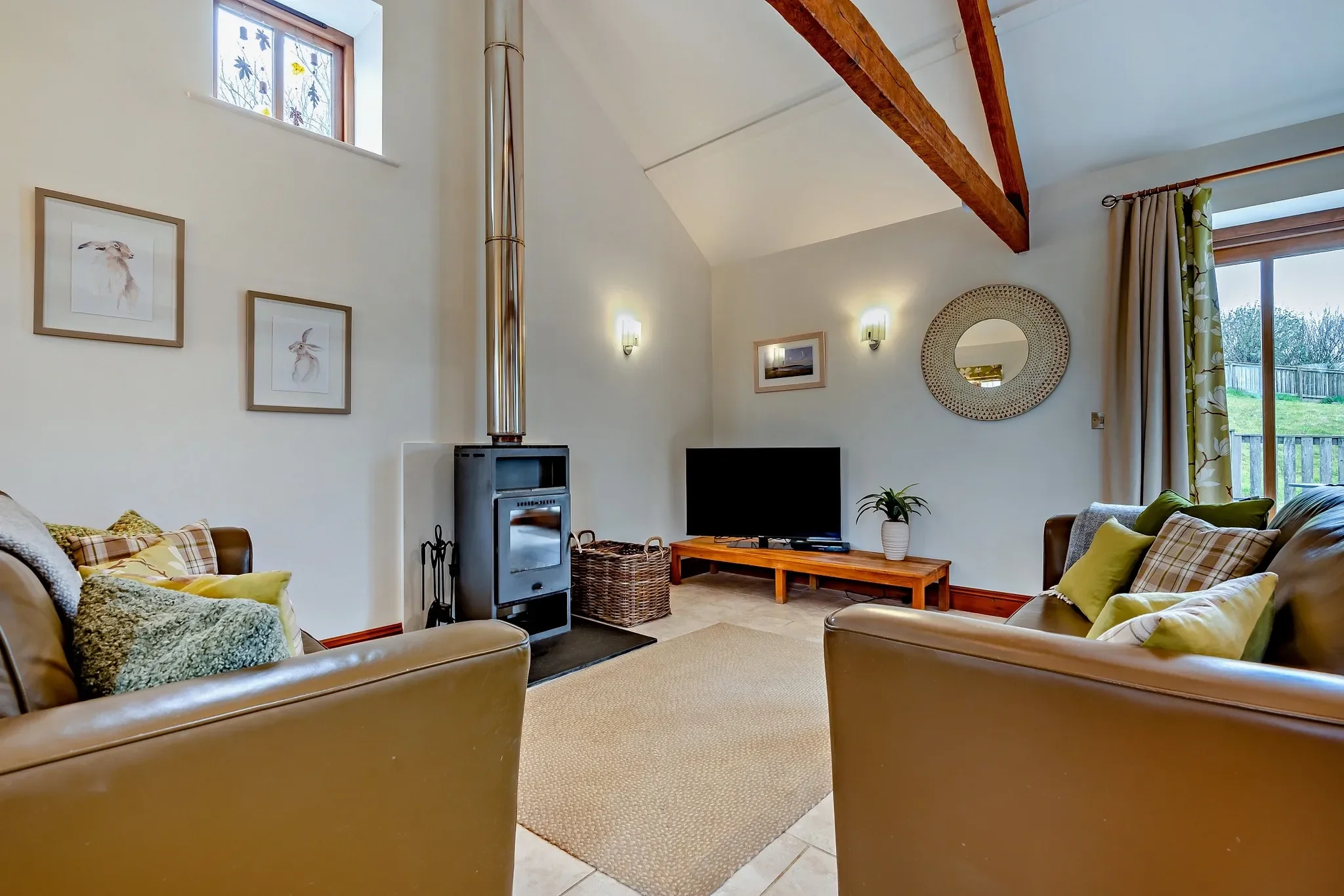 Barley Park lounge with a freestanding wood-burning stove, vaulted ceiling, leather sofas and a flat-screen TV on a timber stand.