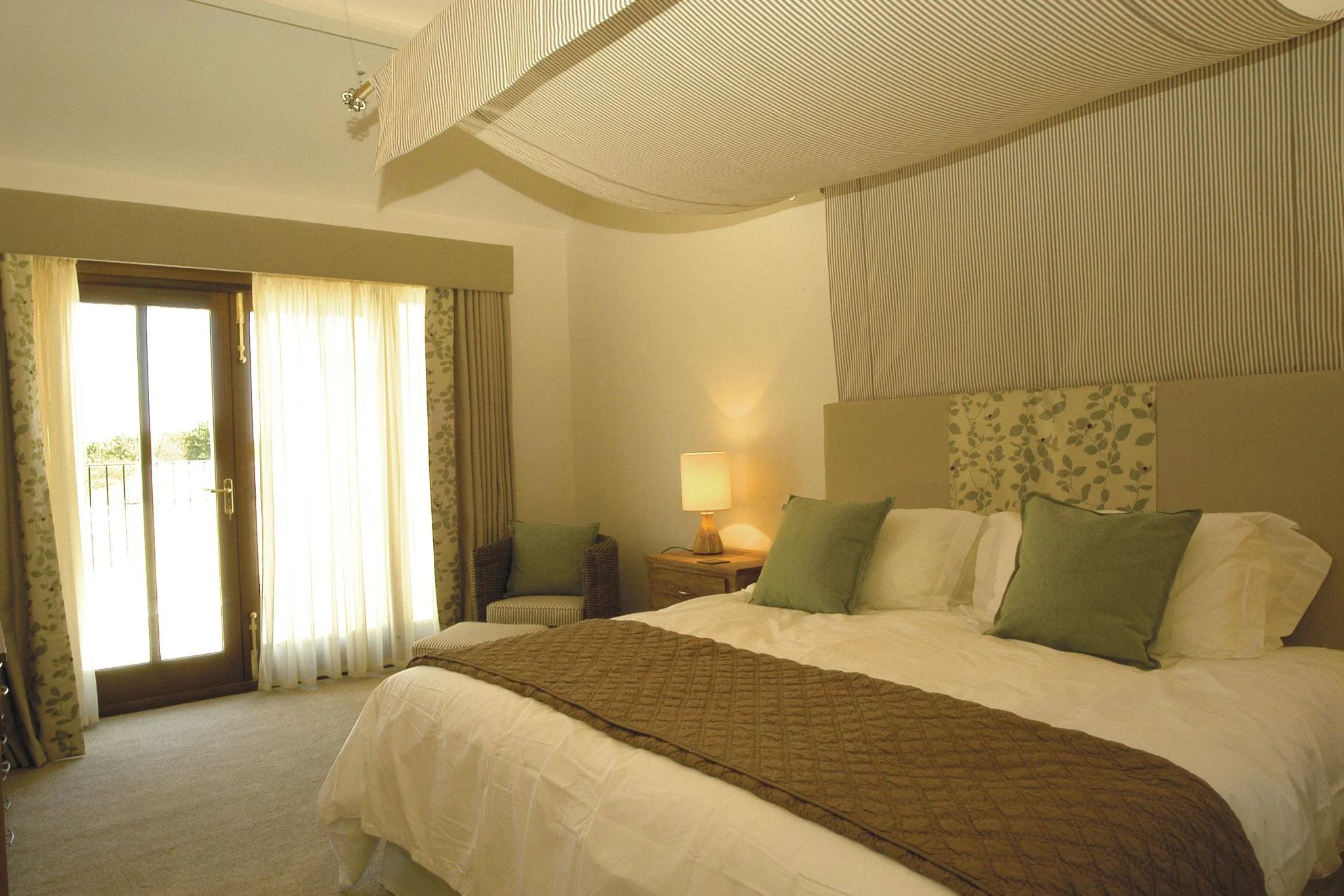 Barley Park master bedroom showing the canopy bed and french doors opening to a private terrace with countryside views beyond.