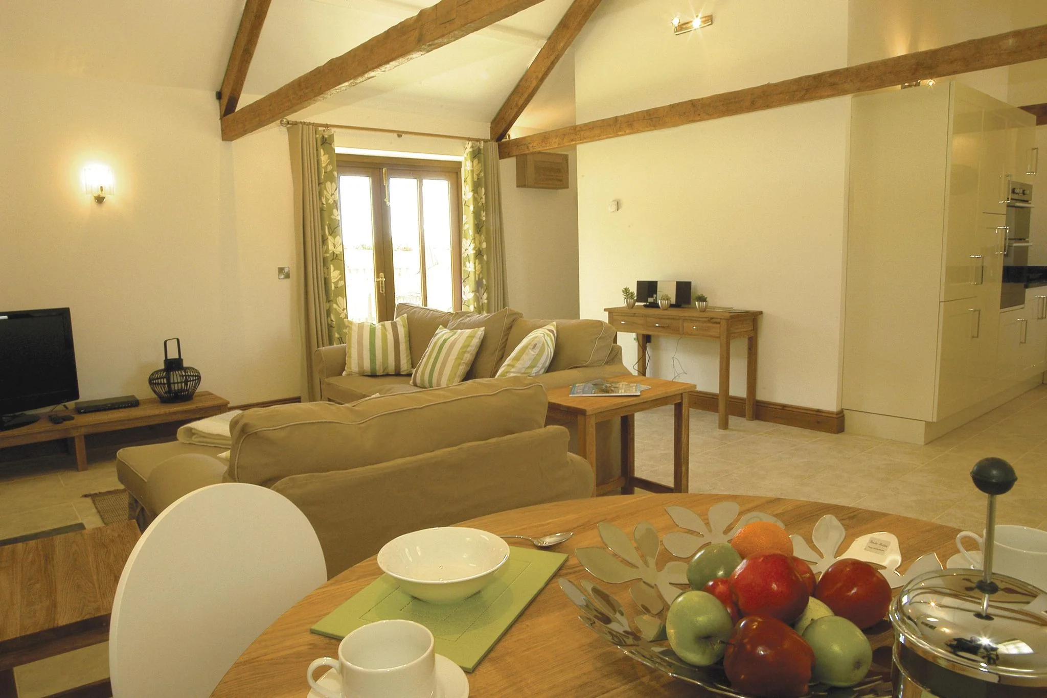 Barley Park open-plan living and dining area with vaulted oak beams, a round dining table and sofas leading through to the kitchen.