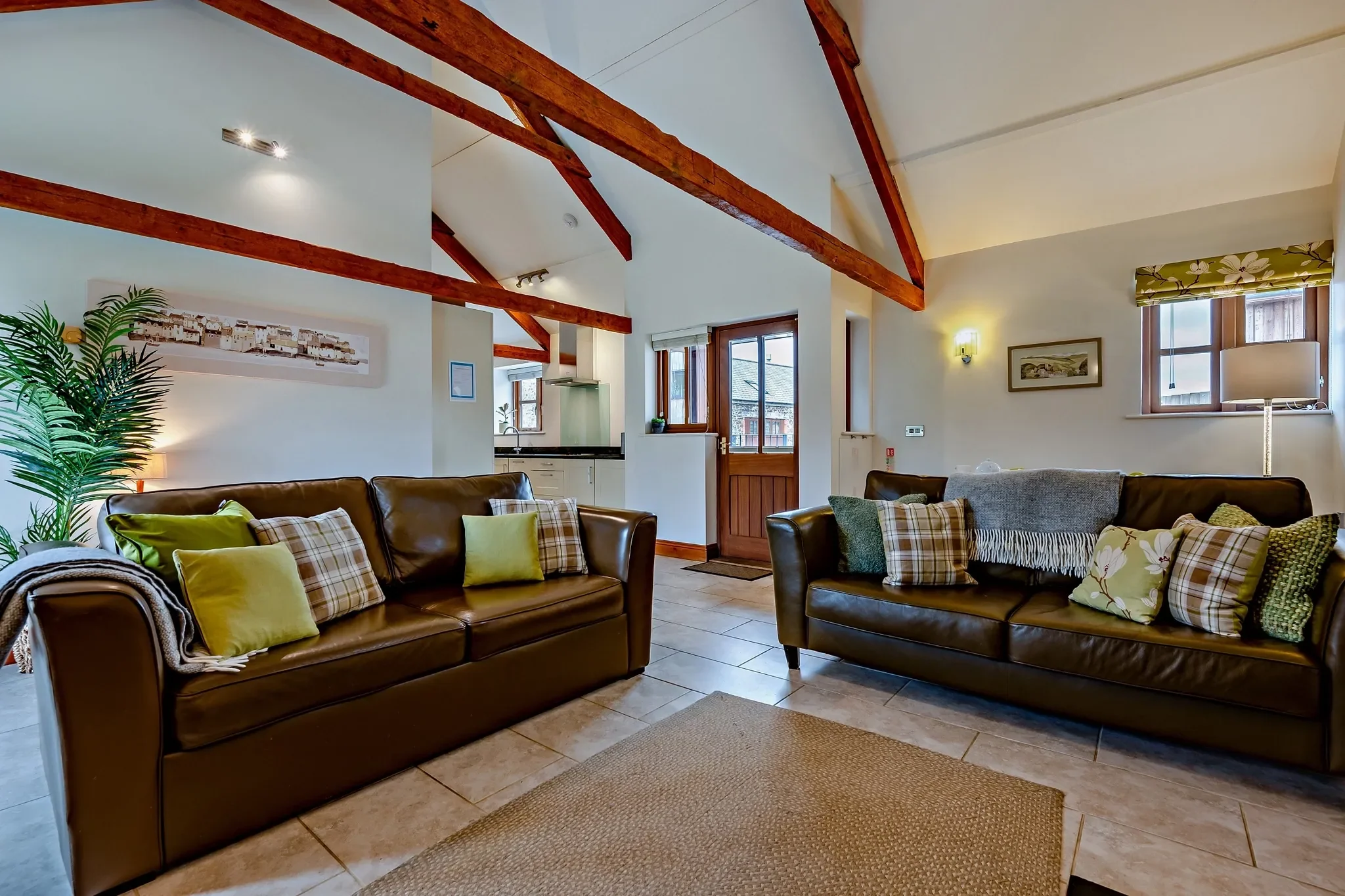 Barley Park open-plan living room with two dark leather sofas under vaulted beams, opening through to the kitchen and front door.