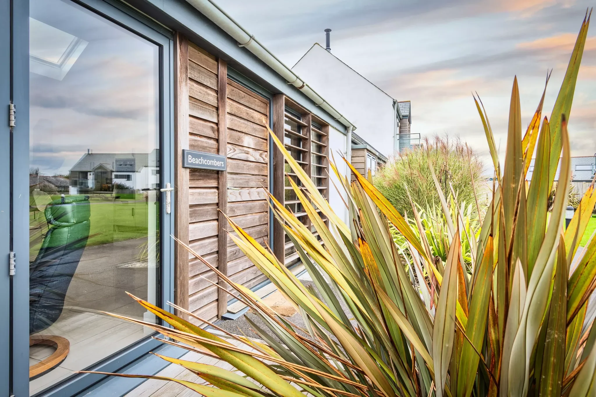 The entrance to Beachcombers, with timber cladding and cordyline planting beside the open glass door