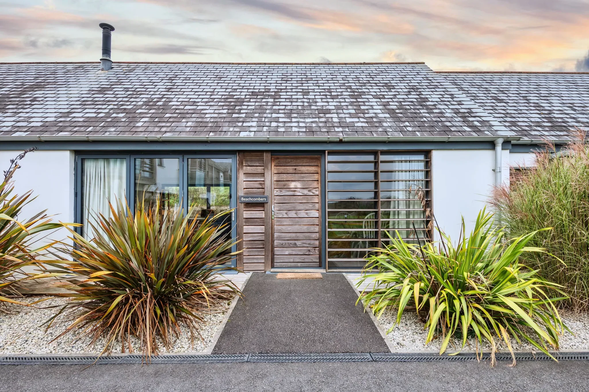 Beachcombers exterior at Whalesborough Farm Resort — timber-clad frontage with planted borders and a paved path to the door