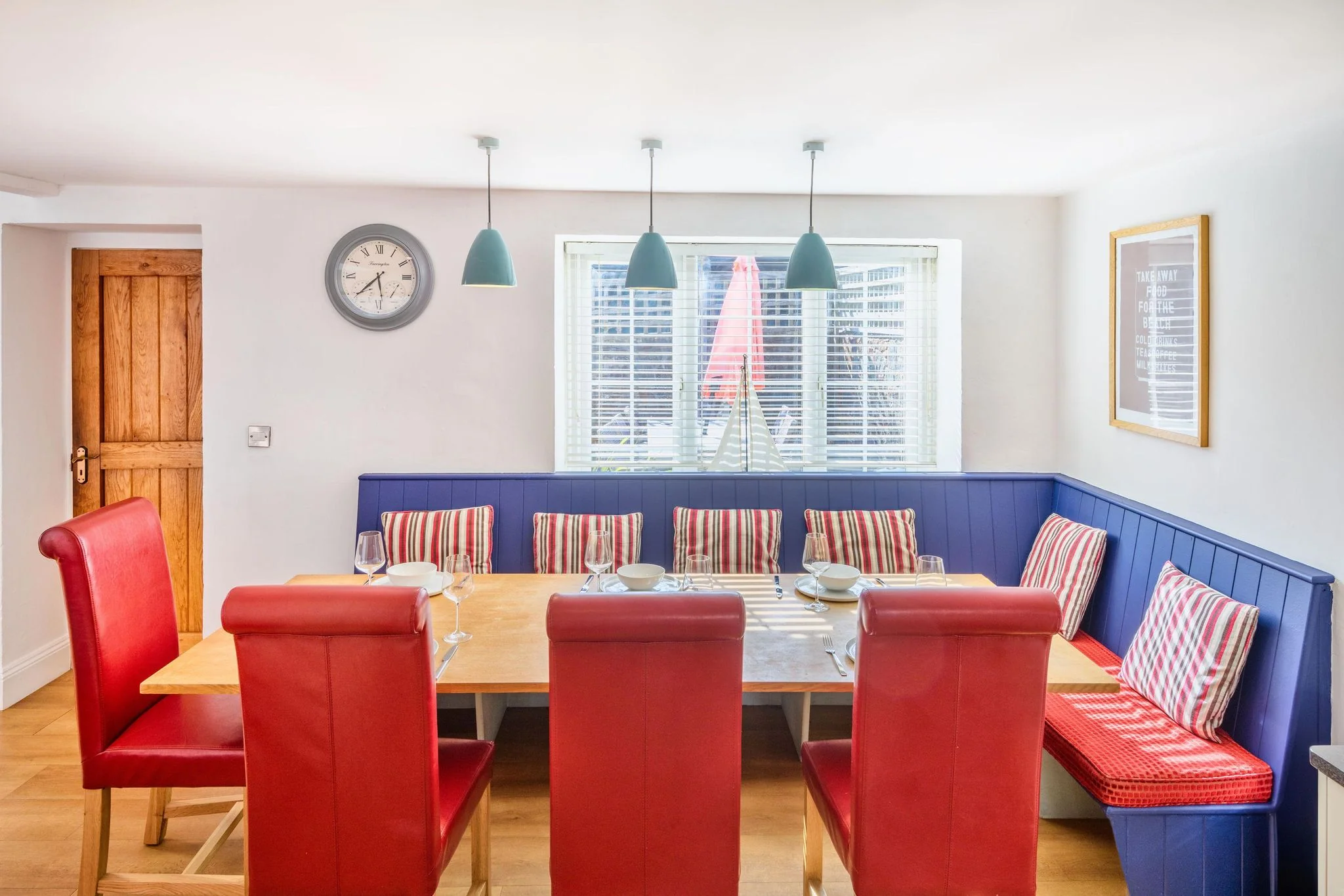 Calf House dining area with large oak table, red high-back chairs, navy banquette seating, and three teal pendant lights above.