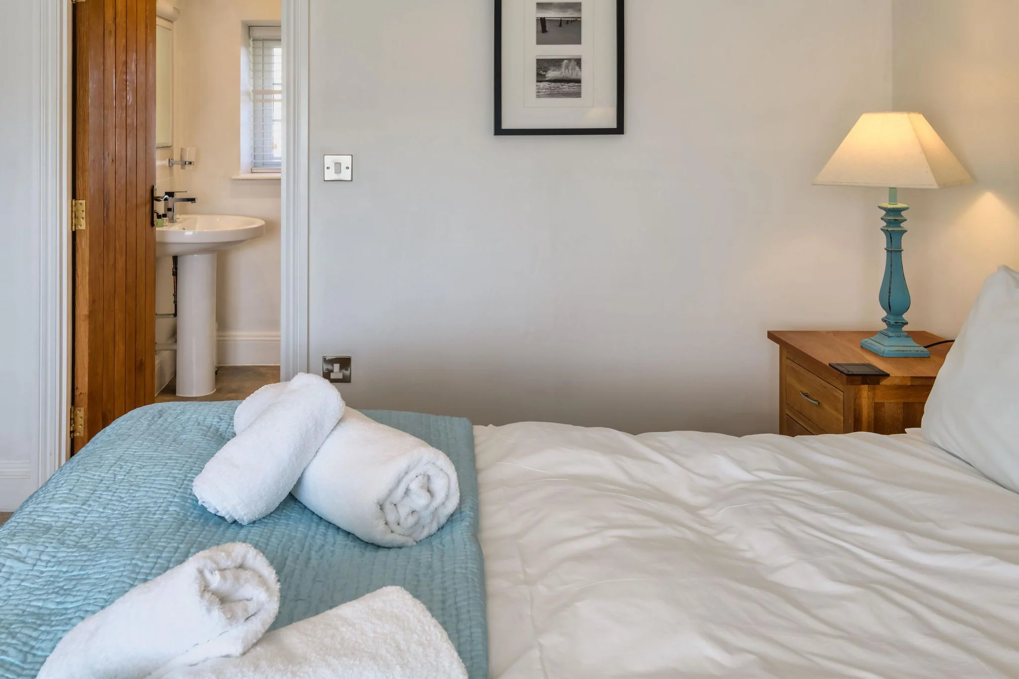 Calf House double bedroom with en-suite bathroom visible through the open door, teal table lamp, and rolled white towels on the bed.