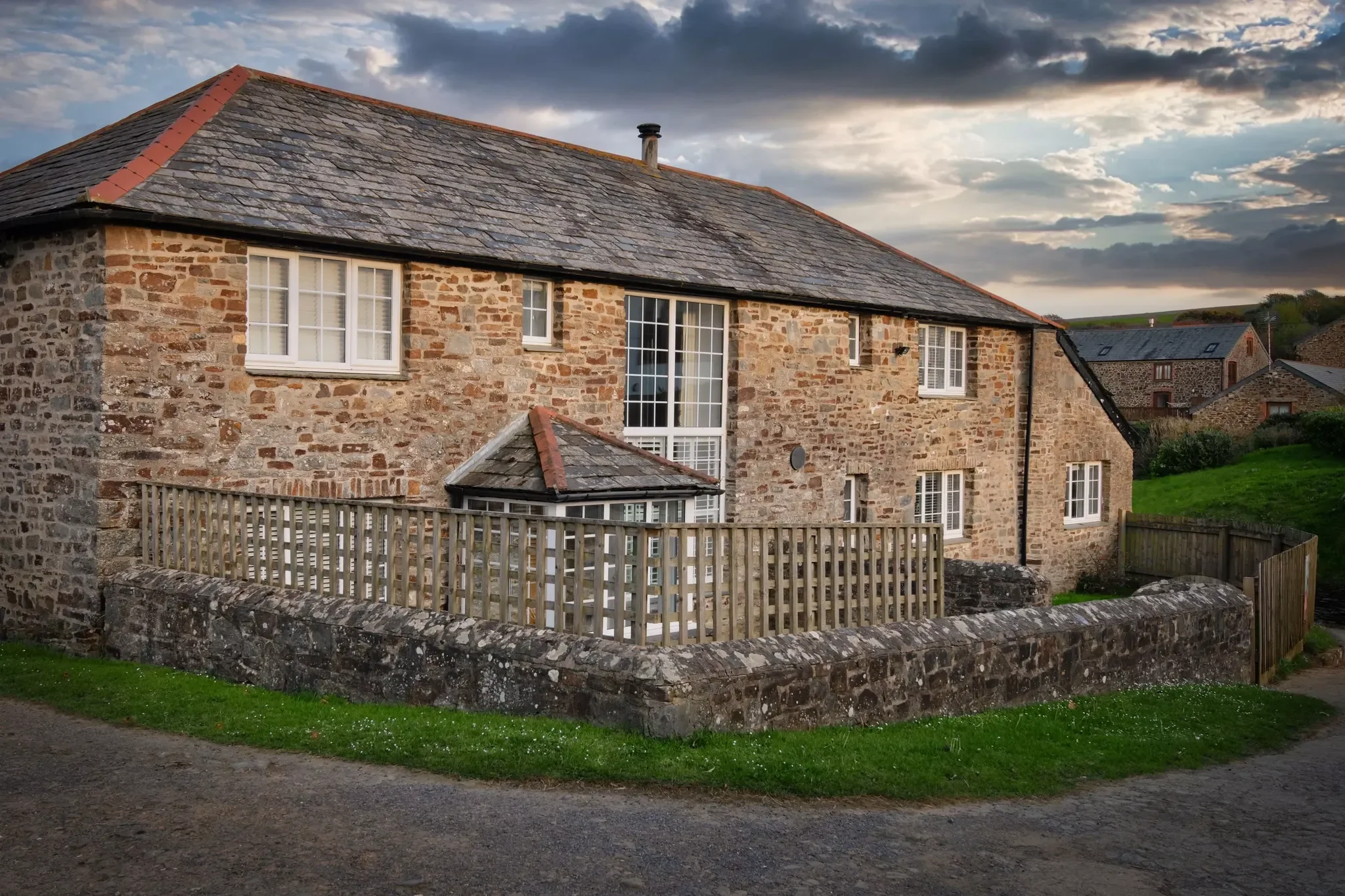 Calf House stone barn conversion at dusk with dramatic clouds, wooden lattice fence, and rolling countryside visible behind.