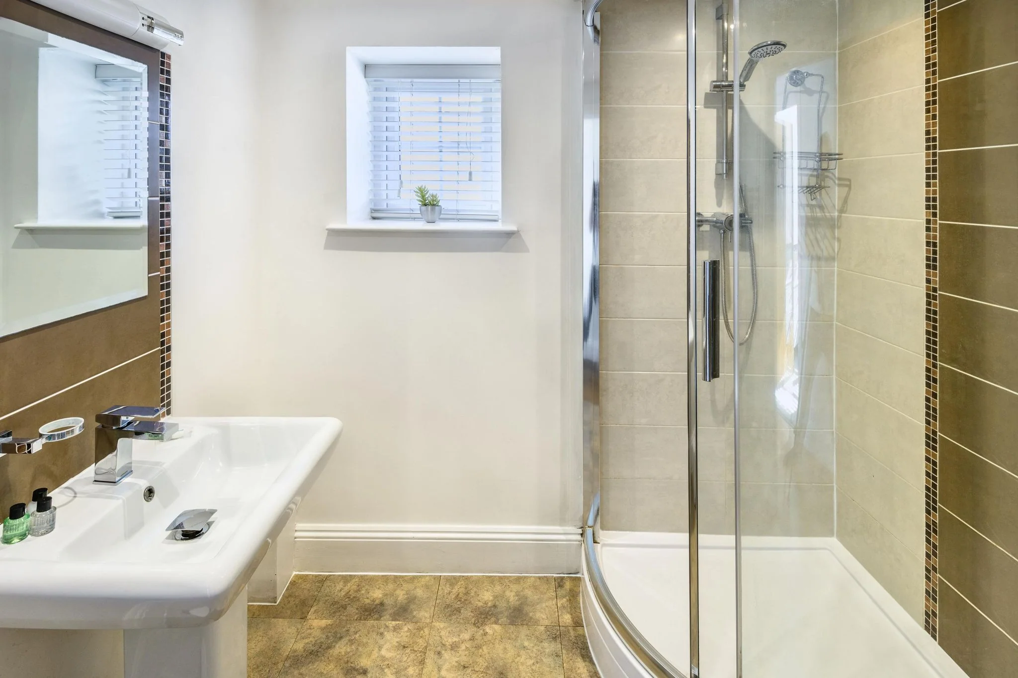 Calf House shower room with curved glass walk-in shower, pedestal basin, mosaic tile borders, and frosted-glass window.