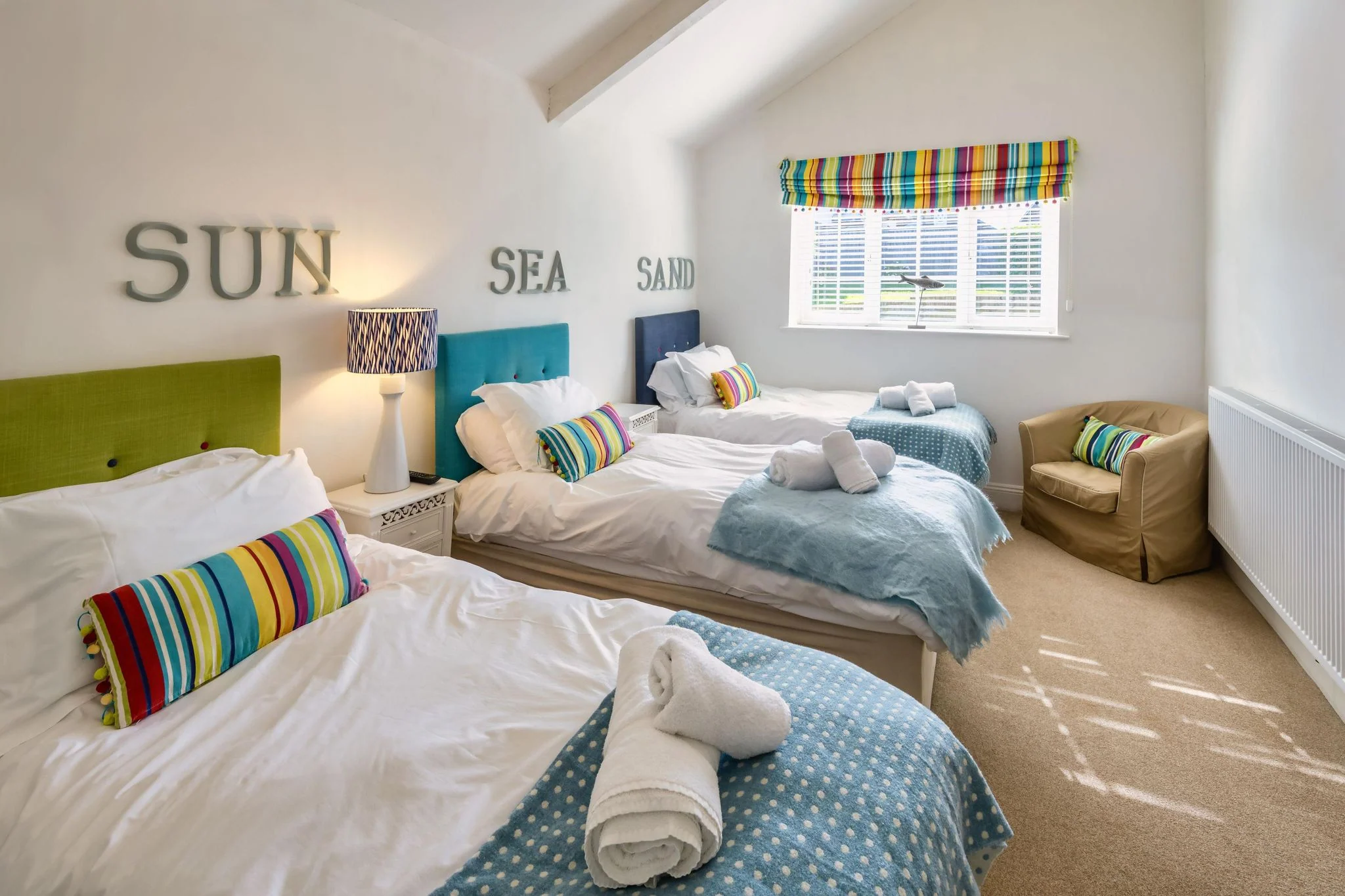 Calf House twin bedroom under the eaves with three single beds, colourful striped cushions, and bright wall lettering.