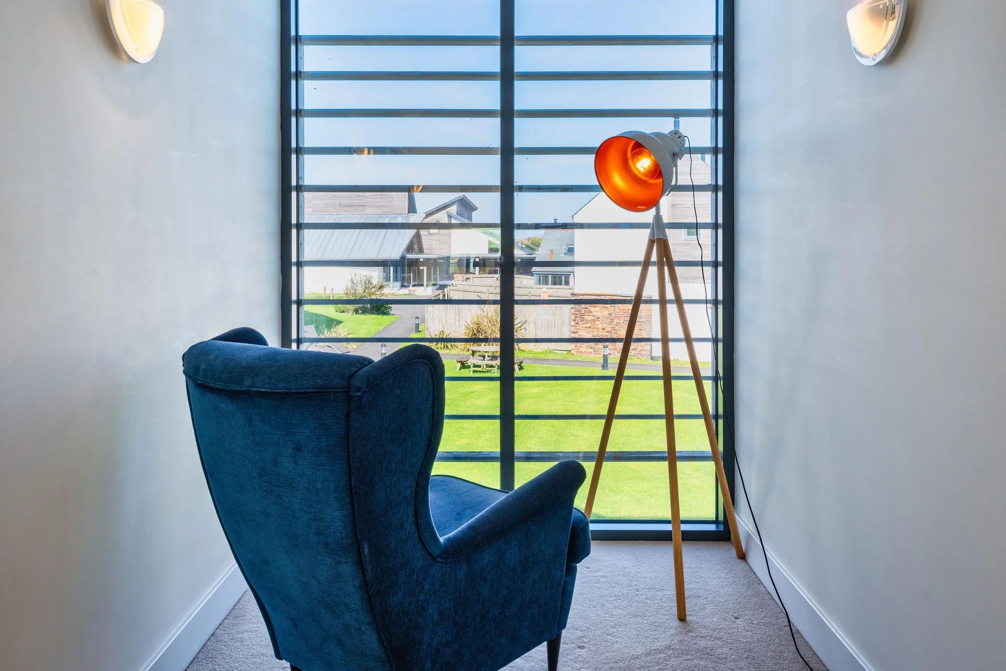 Chapel Park first-floor reading nook with a teal wingback armchair, tripod floor lamp, and tall shuttered window overlooking the estate grounds.