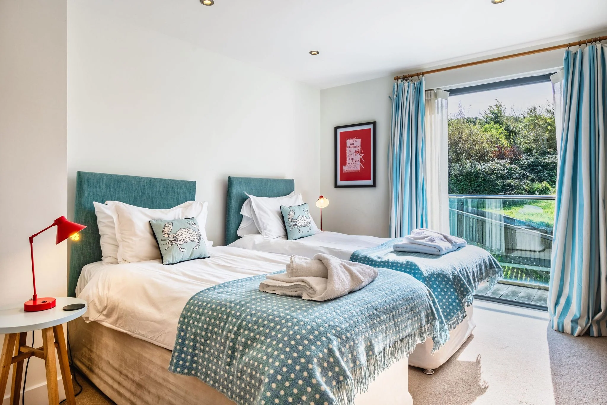 Chapel Park twin bedroom with two teal-upholstered single beds, red bedside lamps, and sliding doors leading out to a private balcony with garden views.