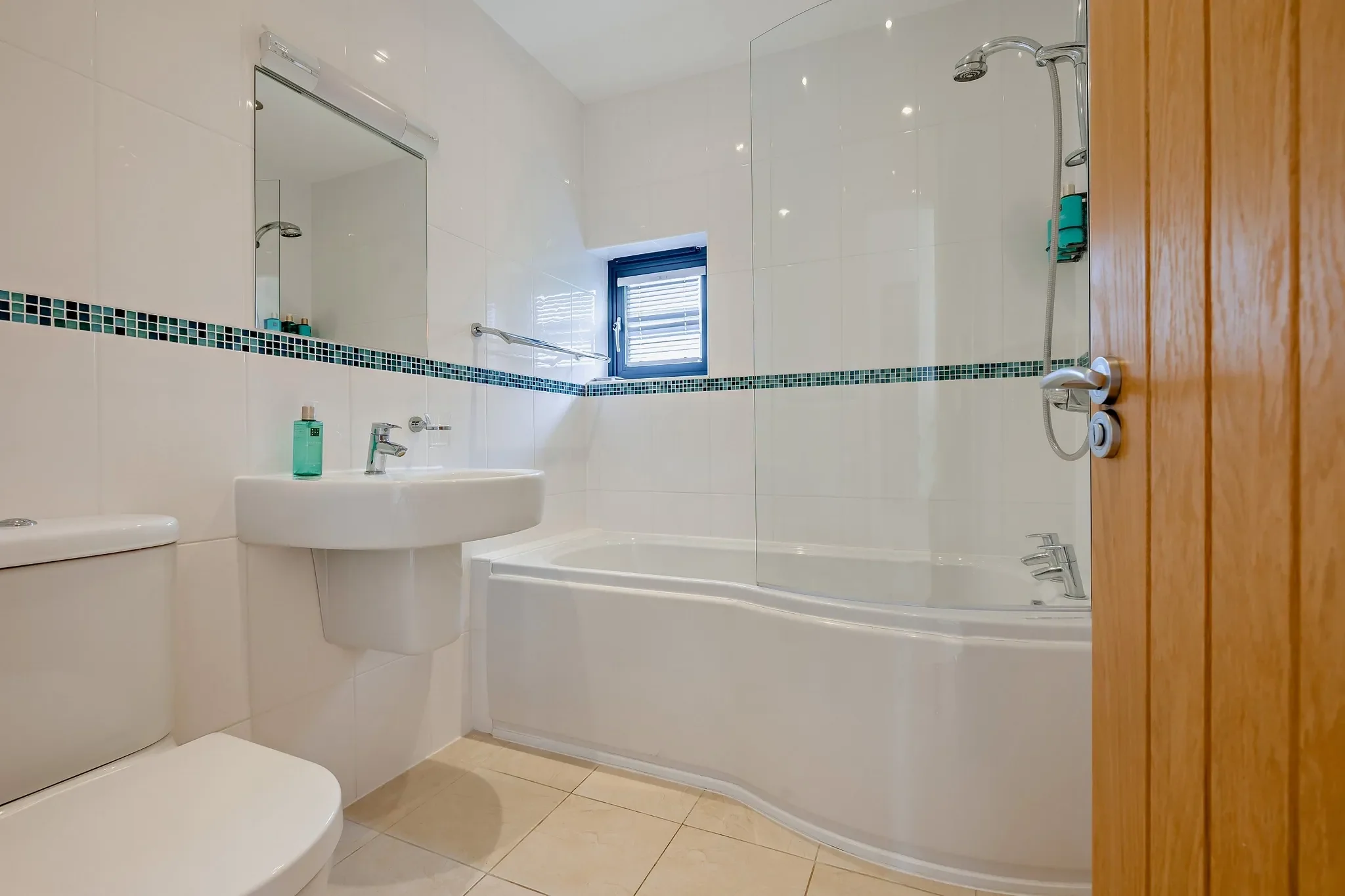 Eagles Nest family bathroom with curved bath, overhead shower, teal mosaic tile border and pedestal basin.