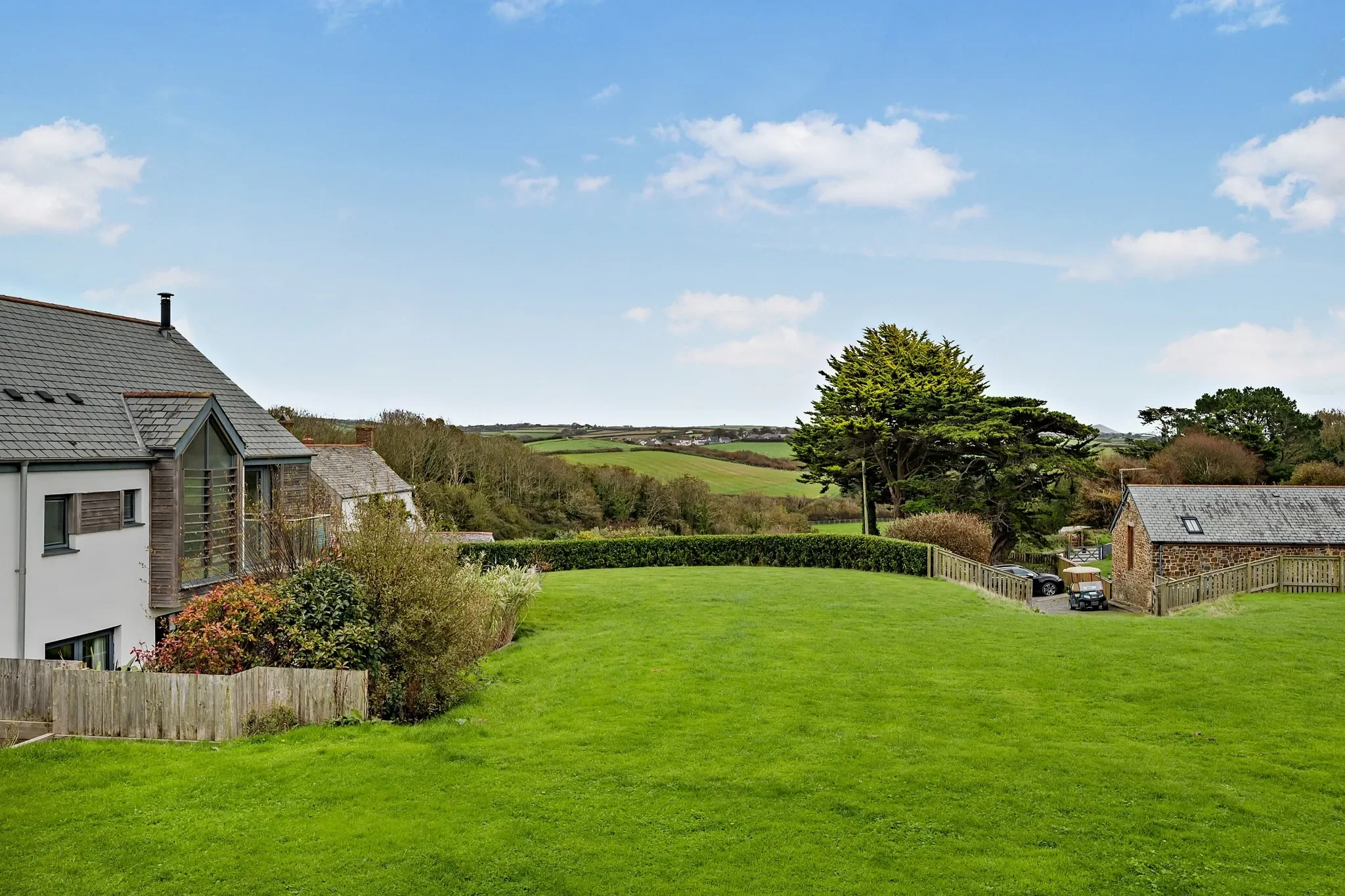 Eagles Nest lawned garden and far-reaching countryside views across the Cornish valley toward rolling green hills.