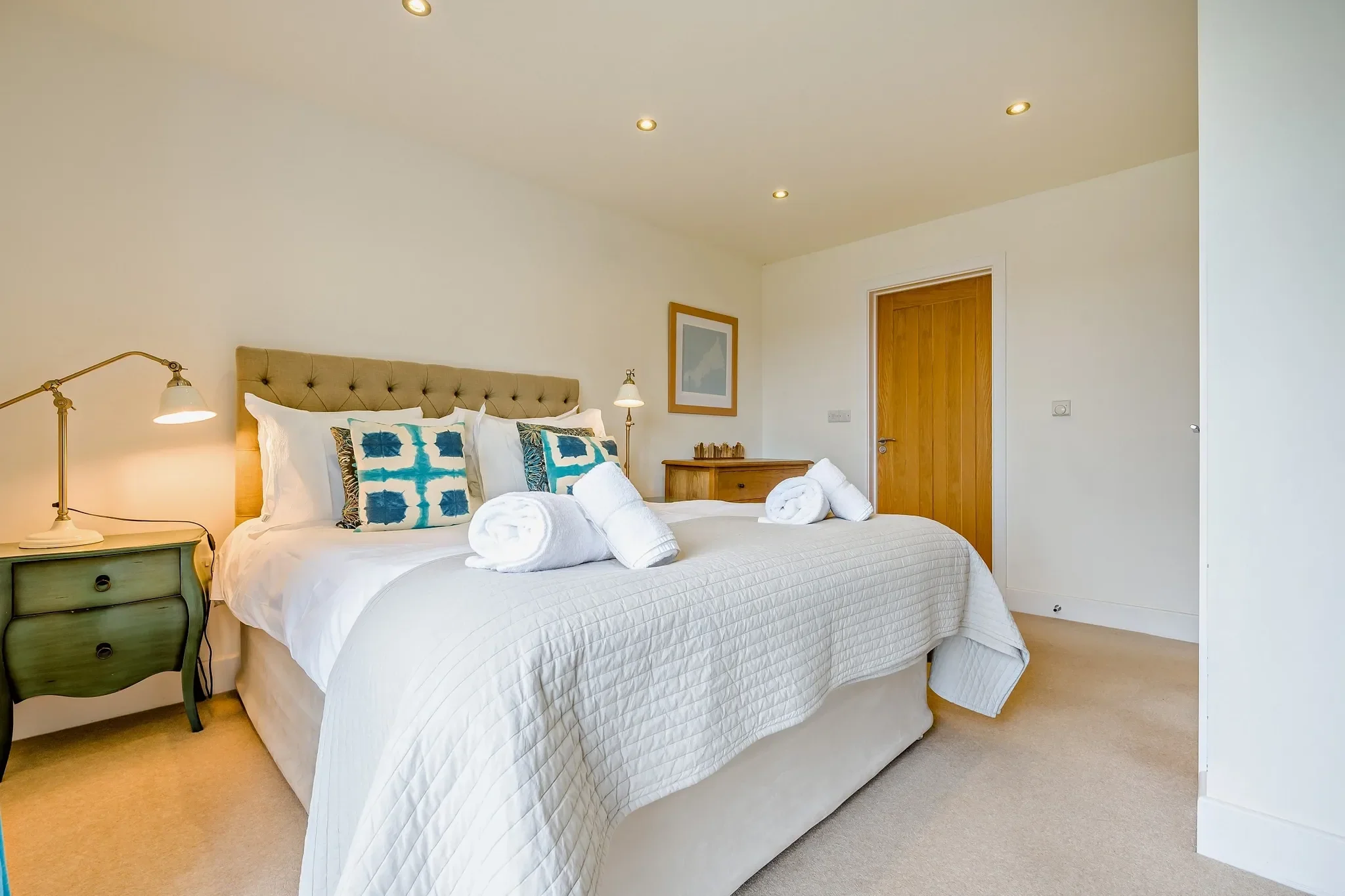 Eagles Nest master bedroom with king-size upholstered bed, teal accent cushions and warm neutral carpeting.