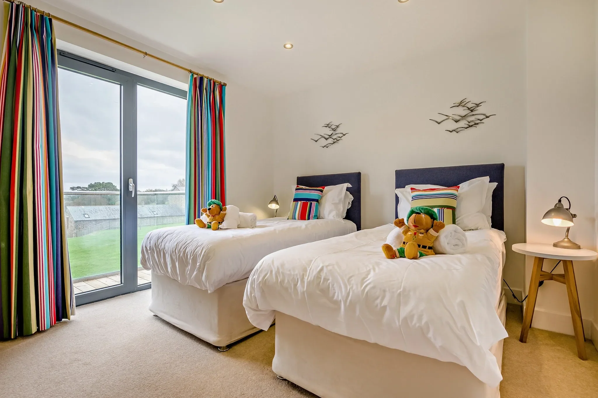 Eagles Nest twin bedroom with two single beds, navy headboards, colourful striped curtains and garden-view French doors.