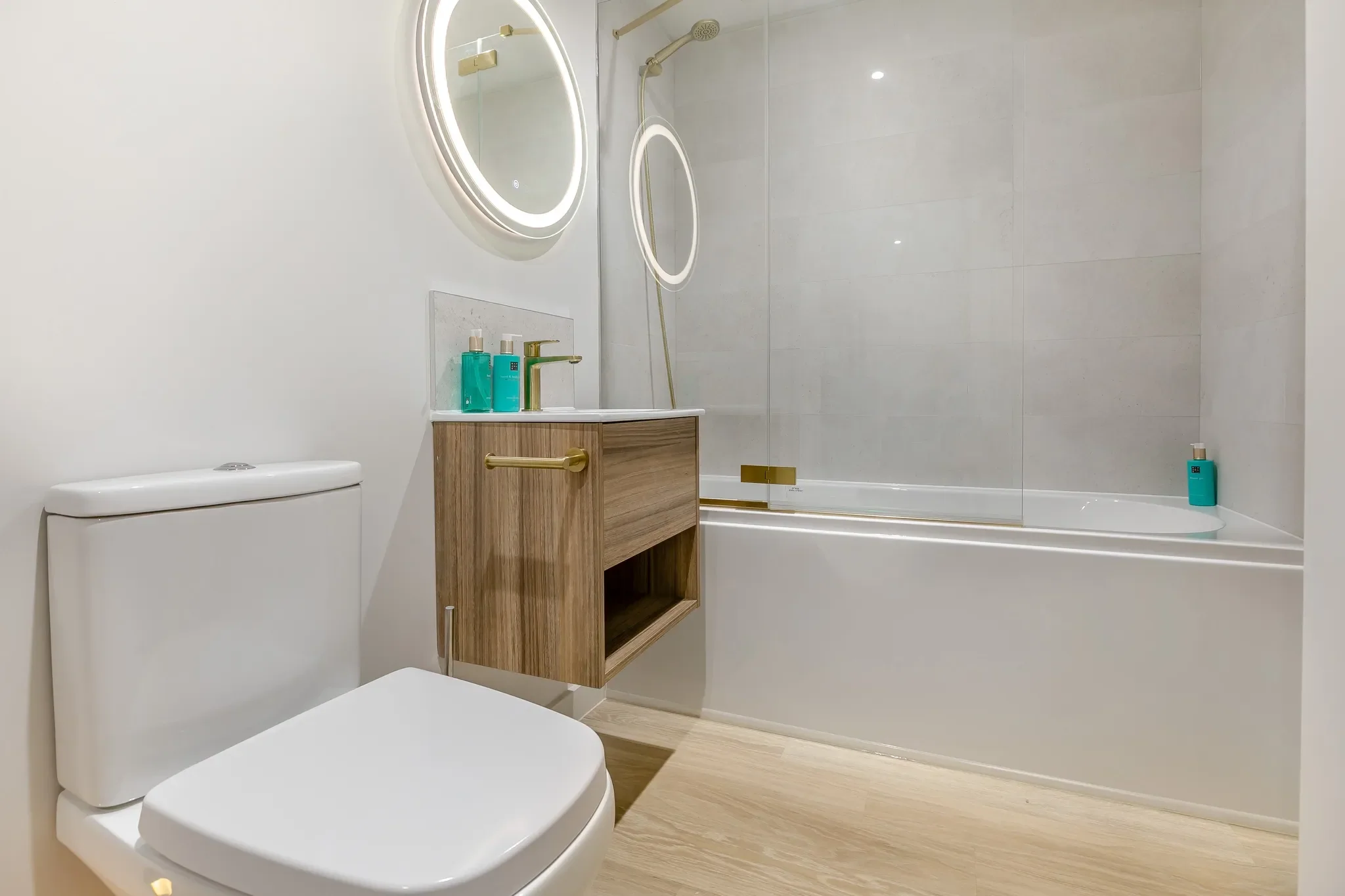 Gwari Spa Barn family bathroom with bath-shower combination, illuminated round mirrors and brass fixtures.