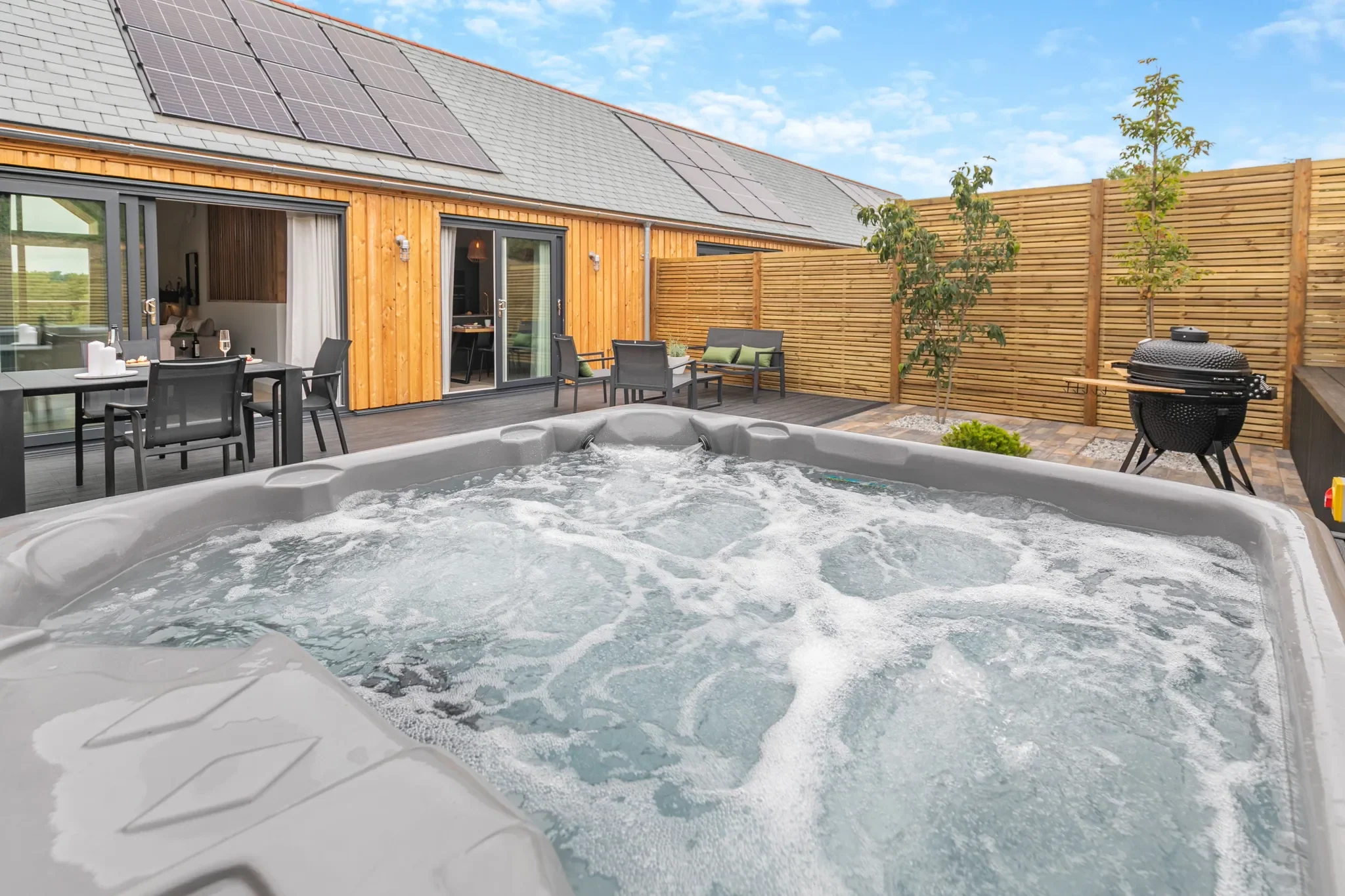 Gwari Spa Barn bubbling hot tub on the private courtyard terrace, with outdoor dining area and kamado grill behind.