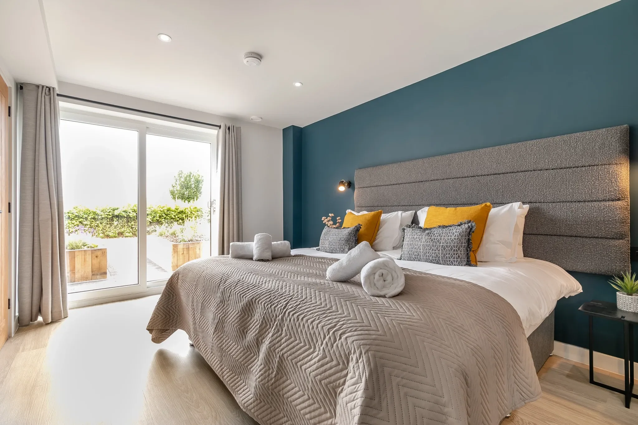 Gwari Spa Barn master bedroom with teal feature wall, king bed, mustard cushions and sliding doors to the terrace.