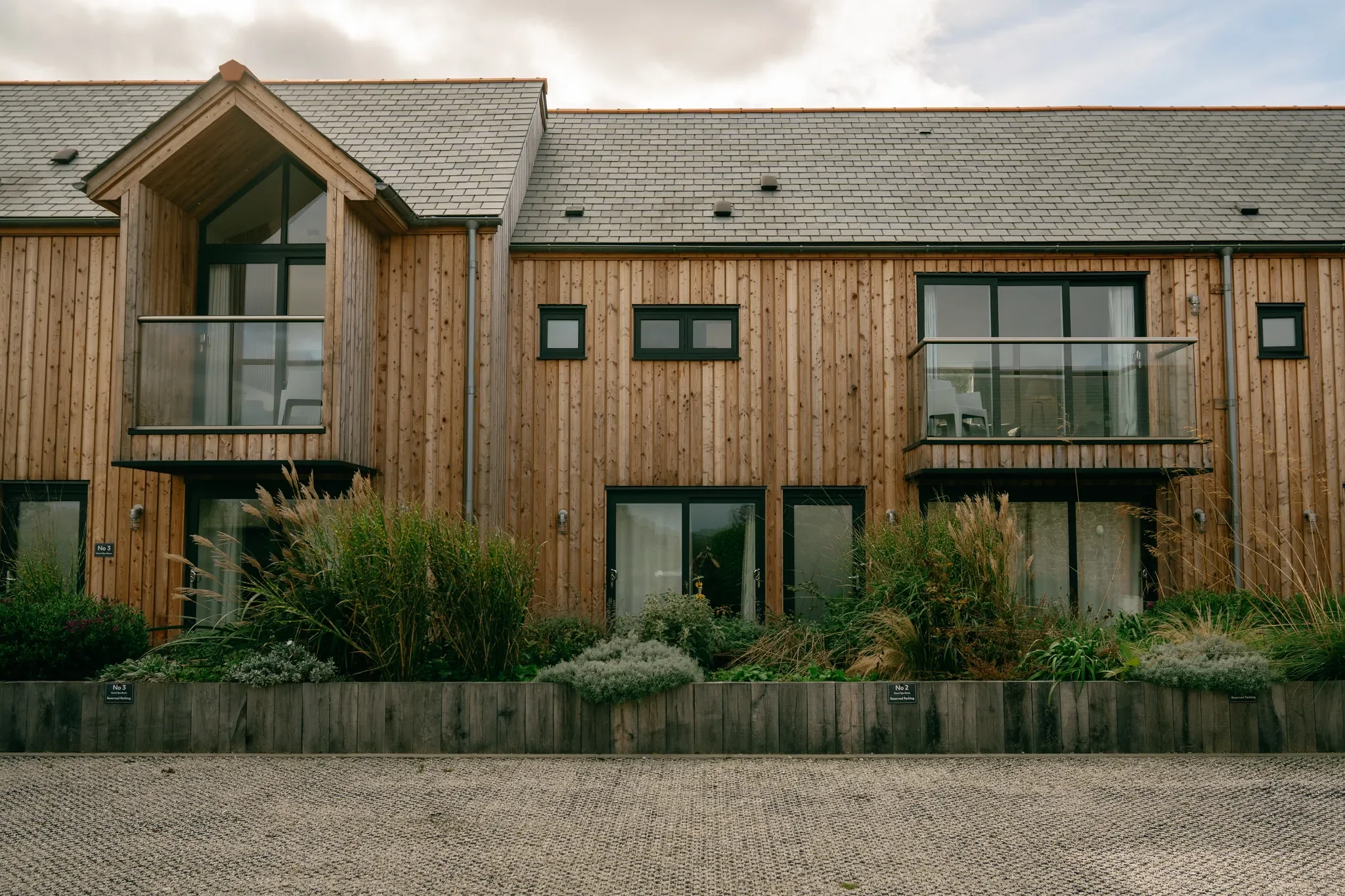 Gwari Spa Barn front elevation of the timber-clad barn conversion with Juliet balconies, ornamental grasses and cobbled forecourt.