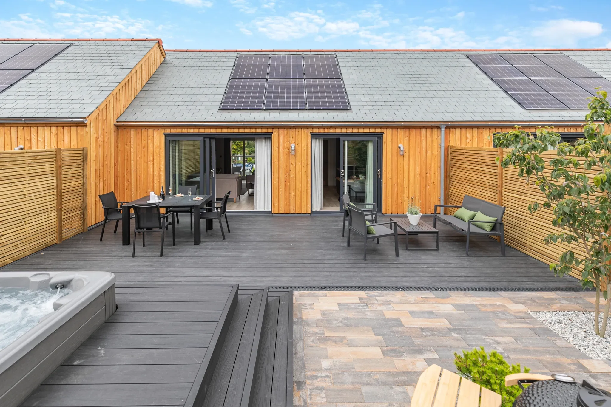 Gwari Spa Barn private terrace and deck viewed from above, showing the hot tub, dining area, lounge seating and solar-panel roof.