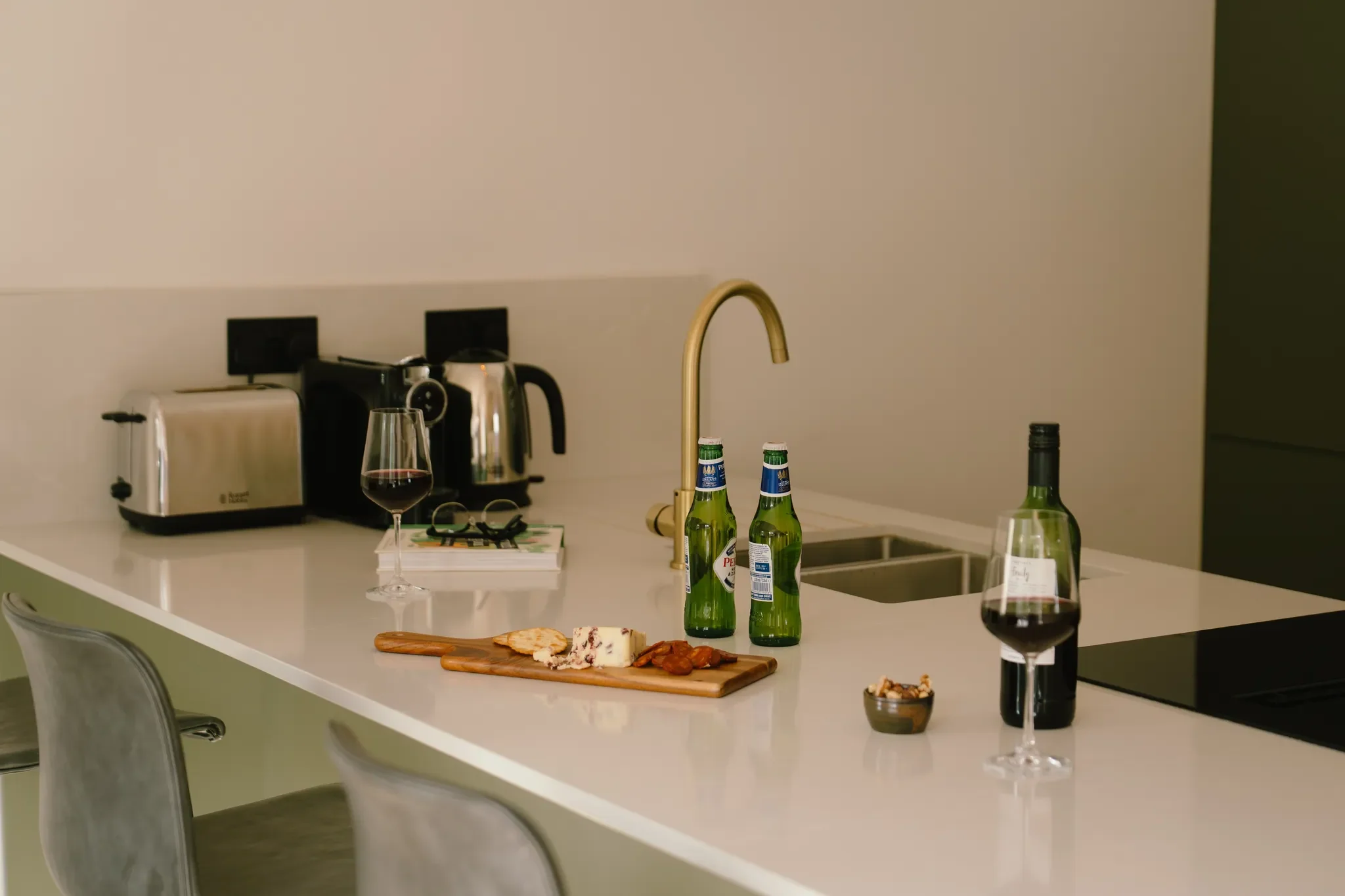 Gwari Spa Barn kitchen island showing the brass arc tap, induction hob, toaster, kettle and cheeseboards laid out along the worktop.