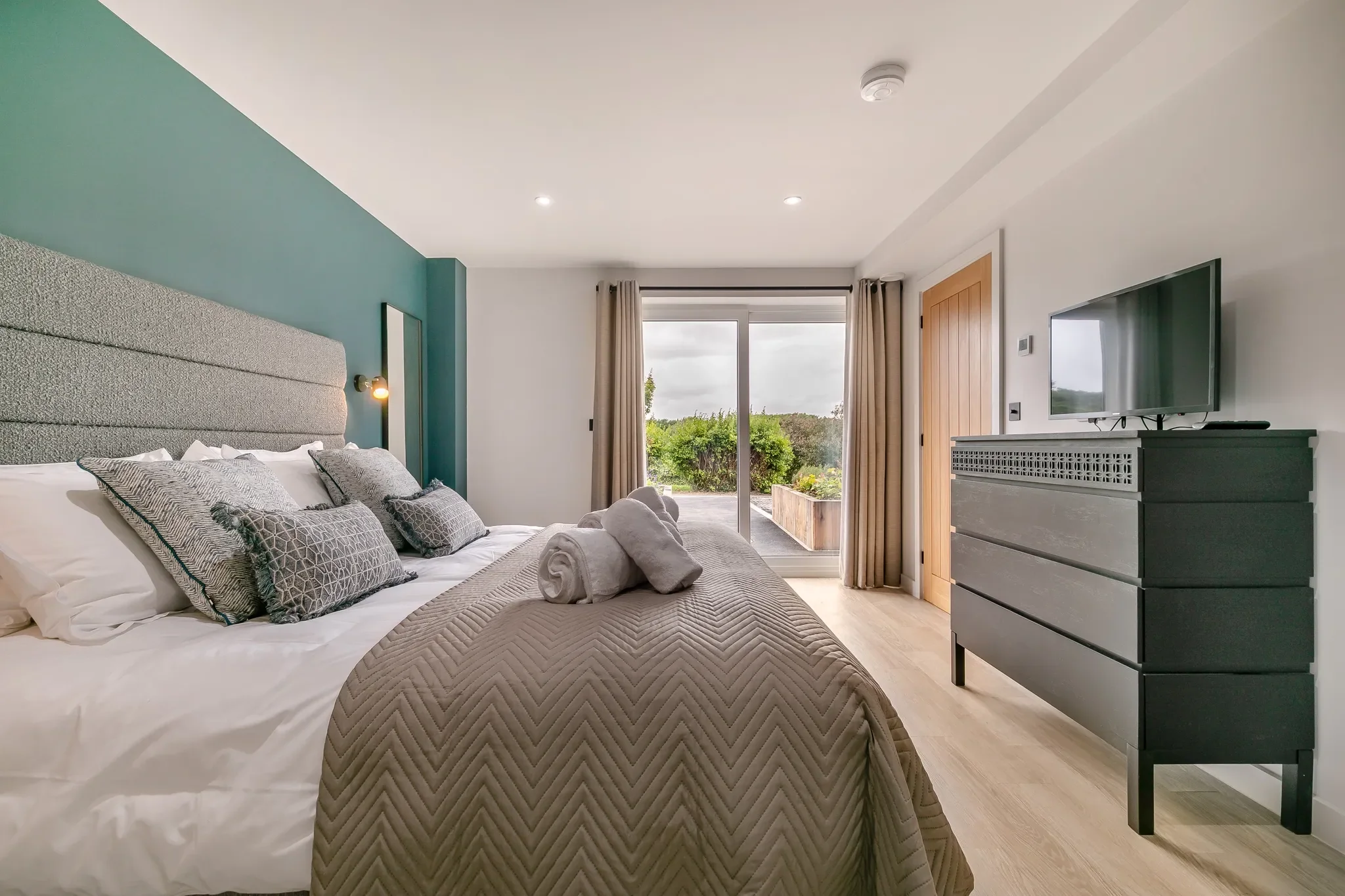 Gwari Spa Barn master bedroom with teal feature wall, king-size bed and sliding doors opening directly onto the terrace.