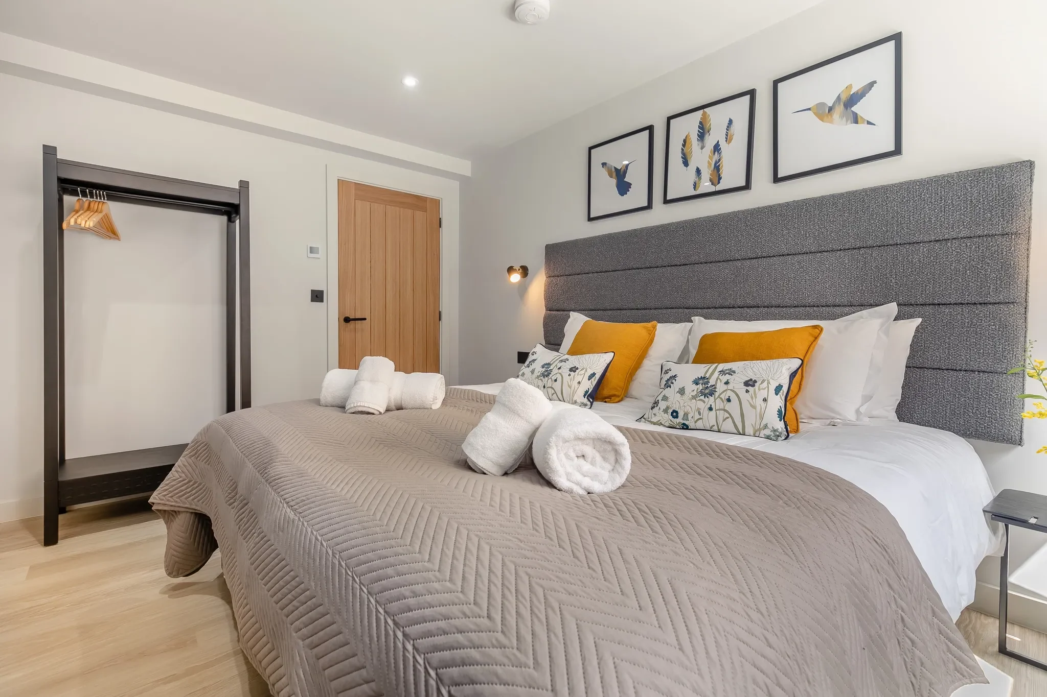 Gwari Spa Barn master bedroom with king-size bed, yellow accent cushions, bird-print artwork and open wardrobe rail.