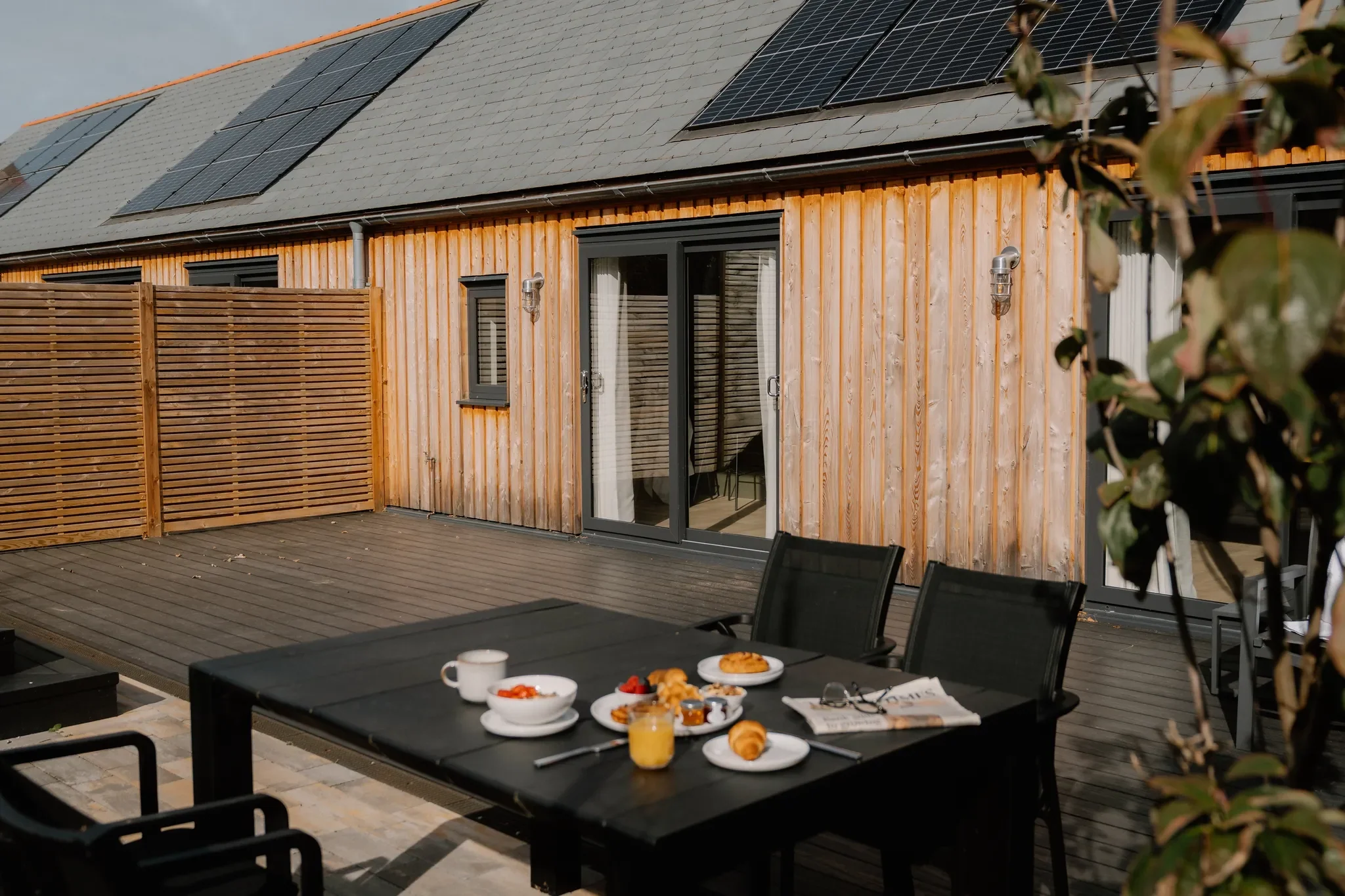 Gwari Spa Barn south-facing terrace with outdoor dining table laid for breakfast and the timber-clad barn facade behind.