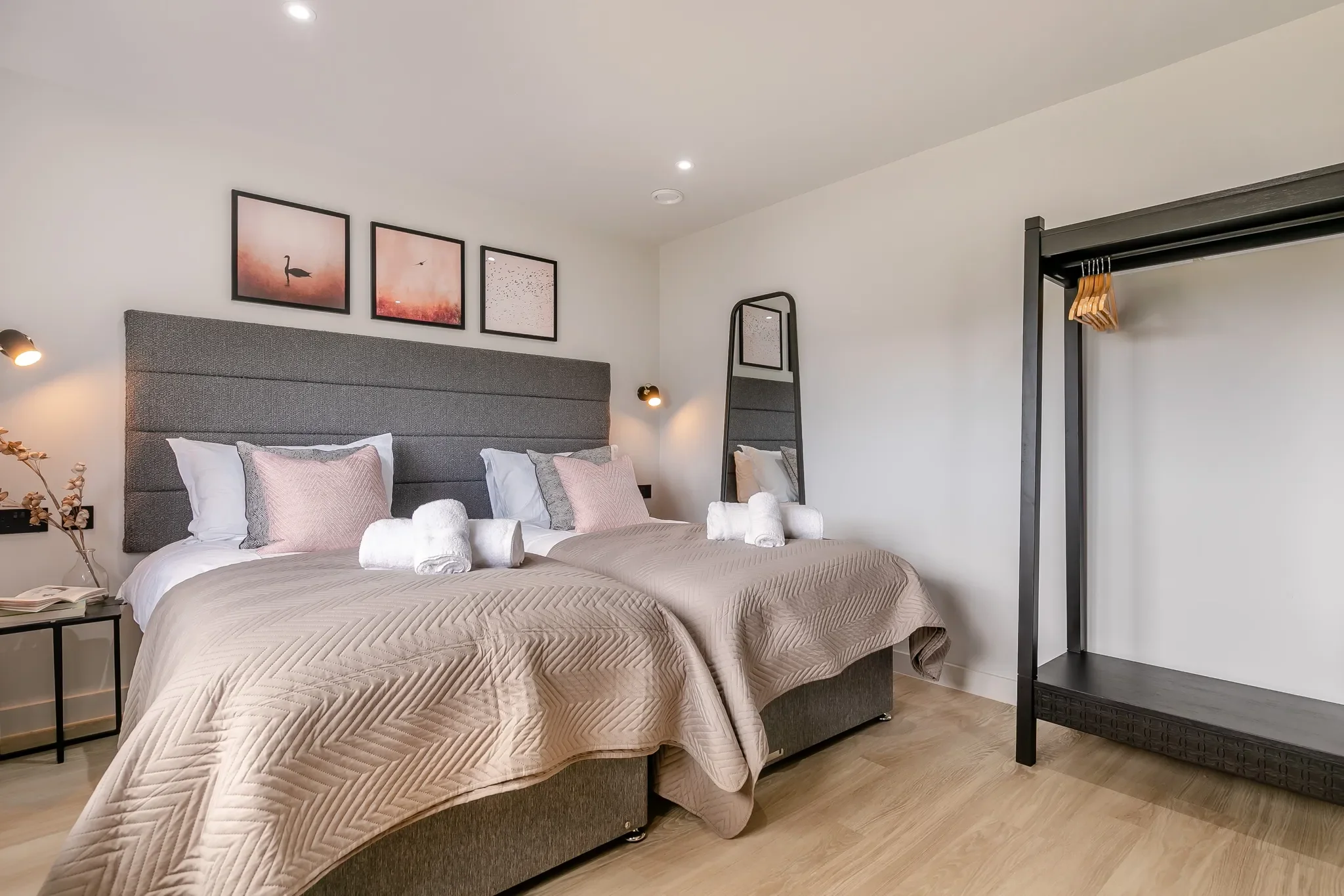 Gwari Spa Barn twin bedroom with two single beds, pink cushions, swan-print artwork and open wardrobe rail.