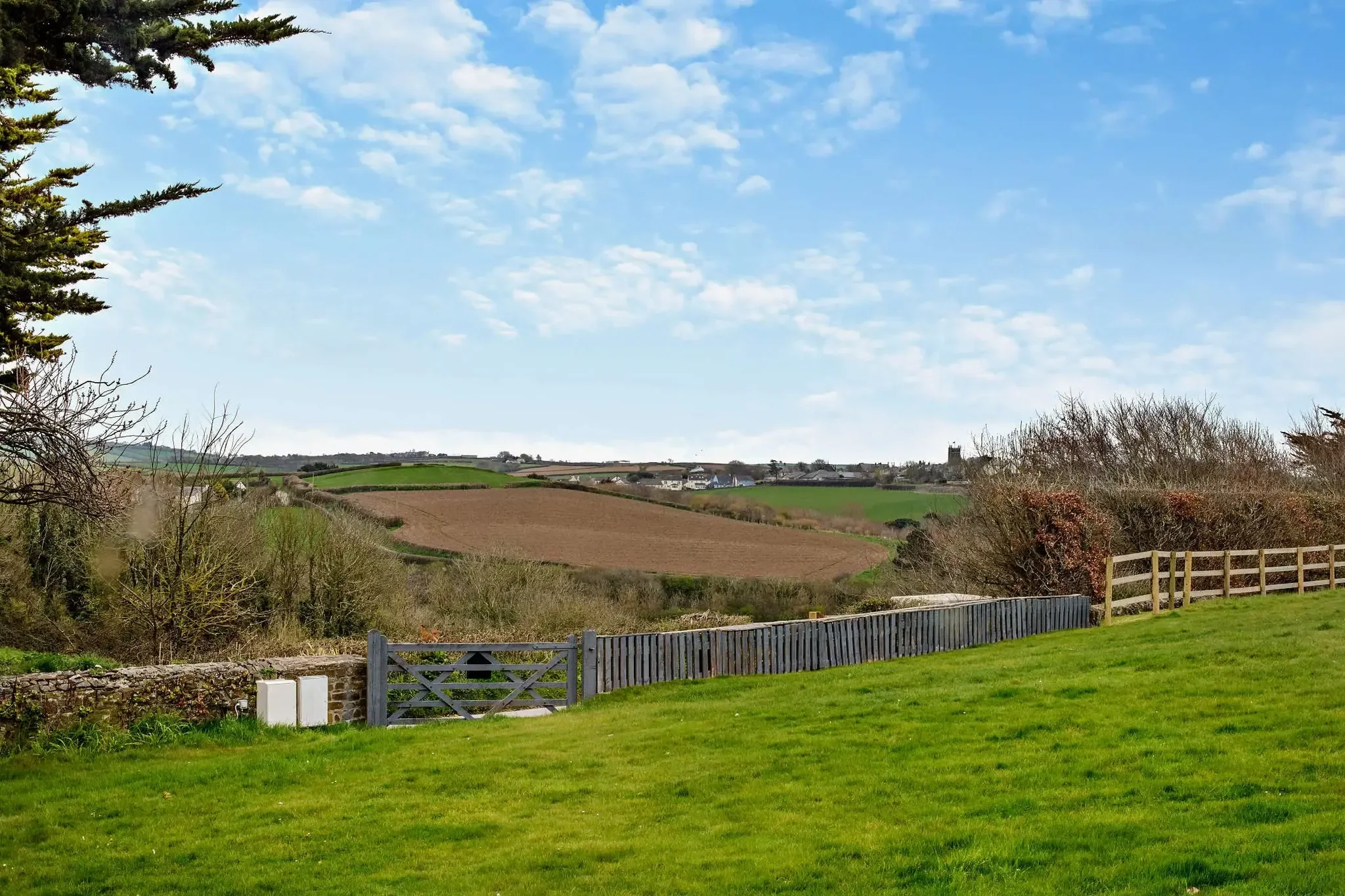 Jack's House garden view across the lawned grounds to open Cornish farmland, distant church tower and wide sky.