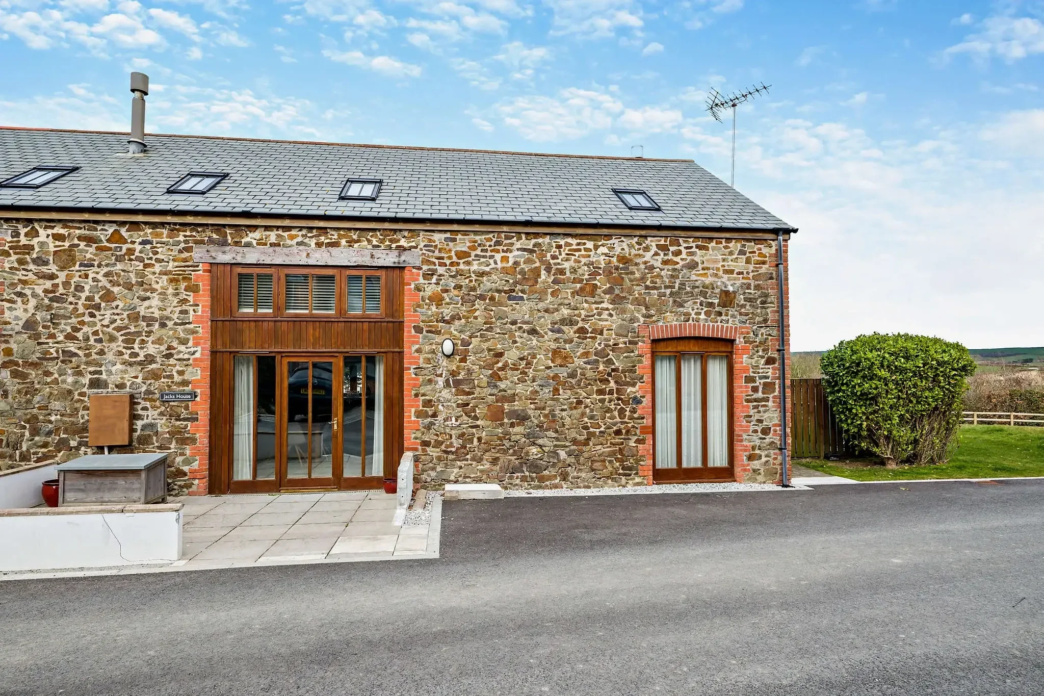 Jack's House stone barn frontage seen straight on, with timber bi-fold doors, slate roof dormers and neatly clipped hedging.