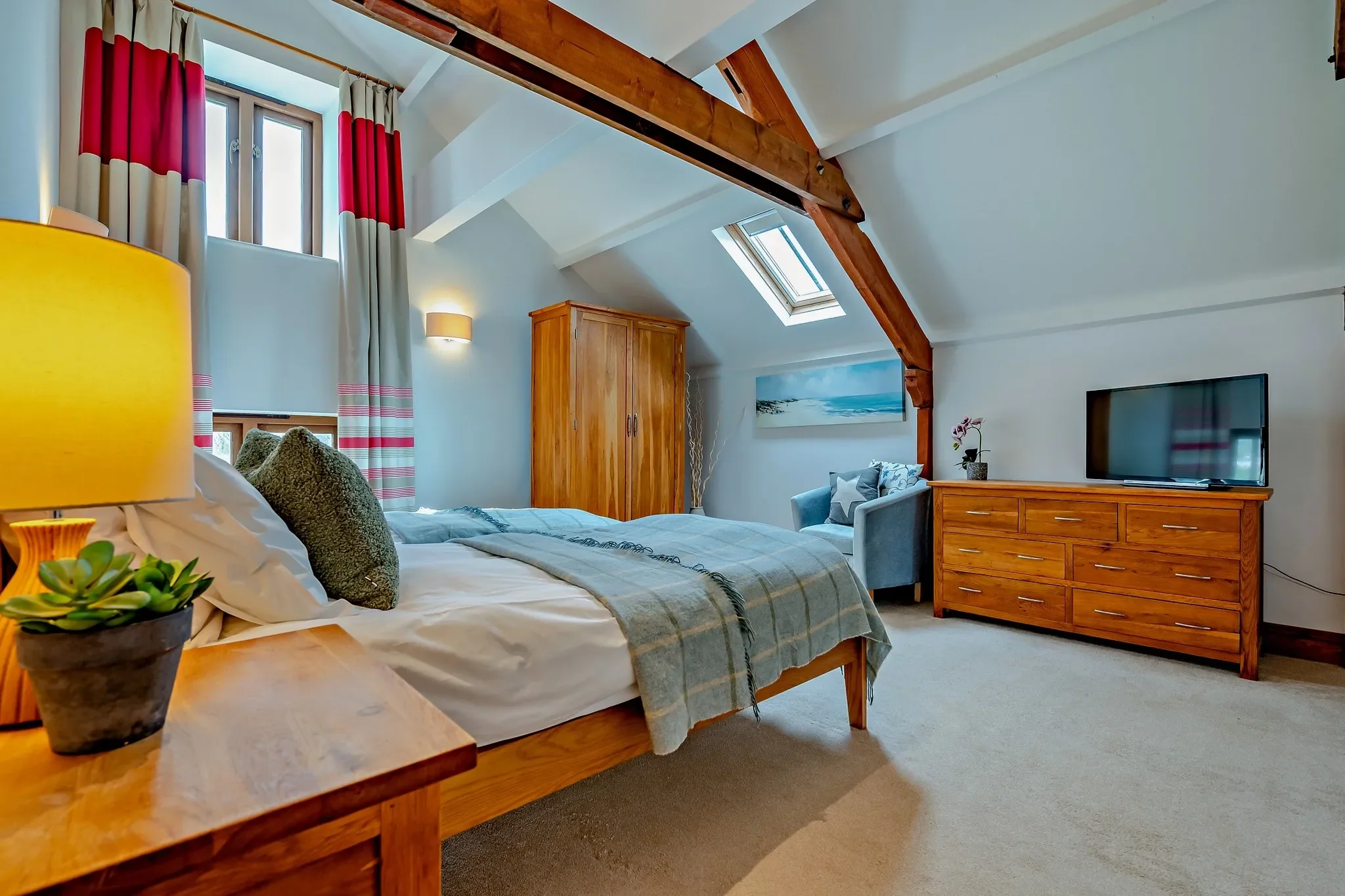 Jack's House master bedroom from the opposite angle showing the oak chest, wall-mounted TV and blue armchair beneath the skylight.