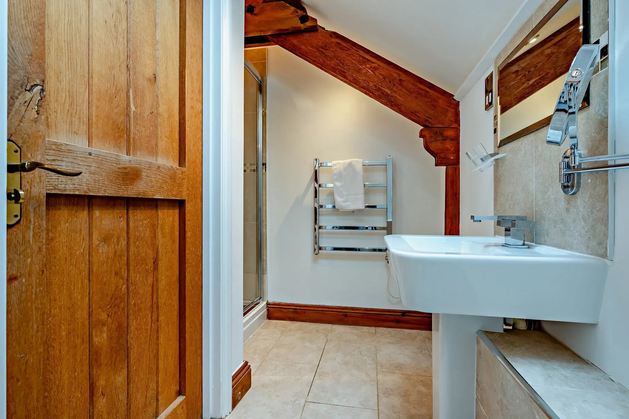 Jack's House upstairs shower room with pedestal basin, heated towel rail and walk-in shower enclosed beneath a sloping beamed ceiling.