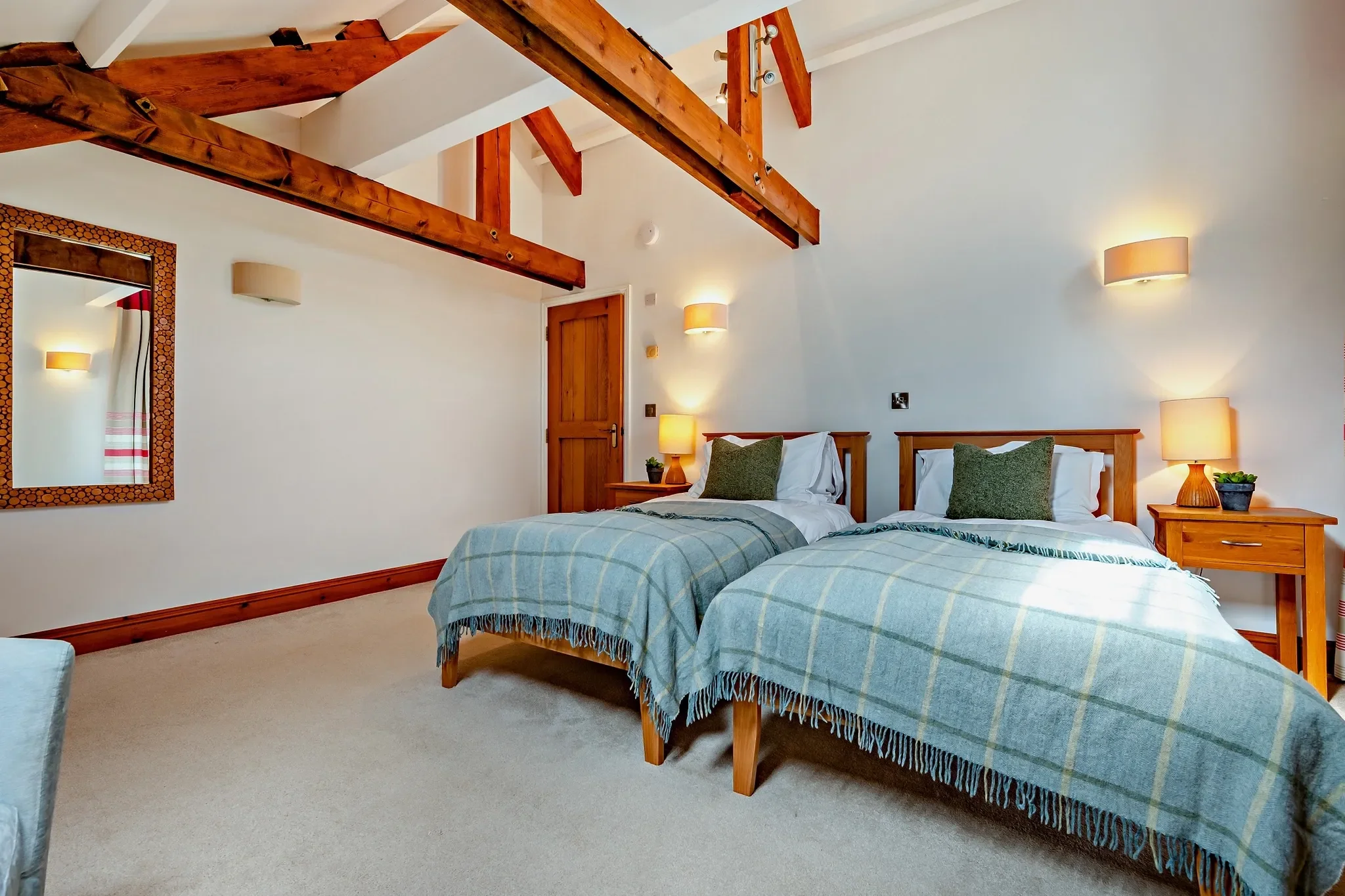 Jack's House twin bedroom with two single beds dressed in check throws, exposed roof beams and warm wall lighting.