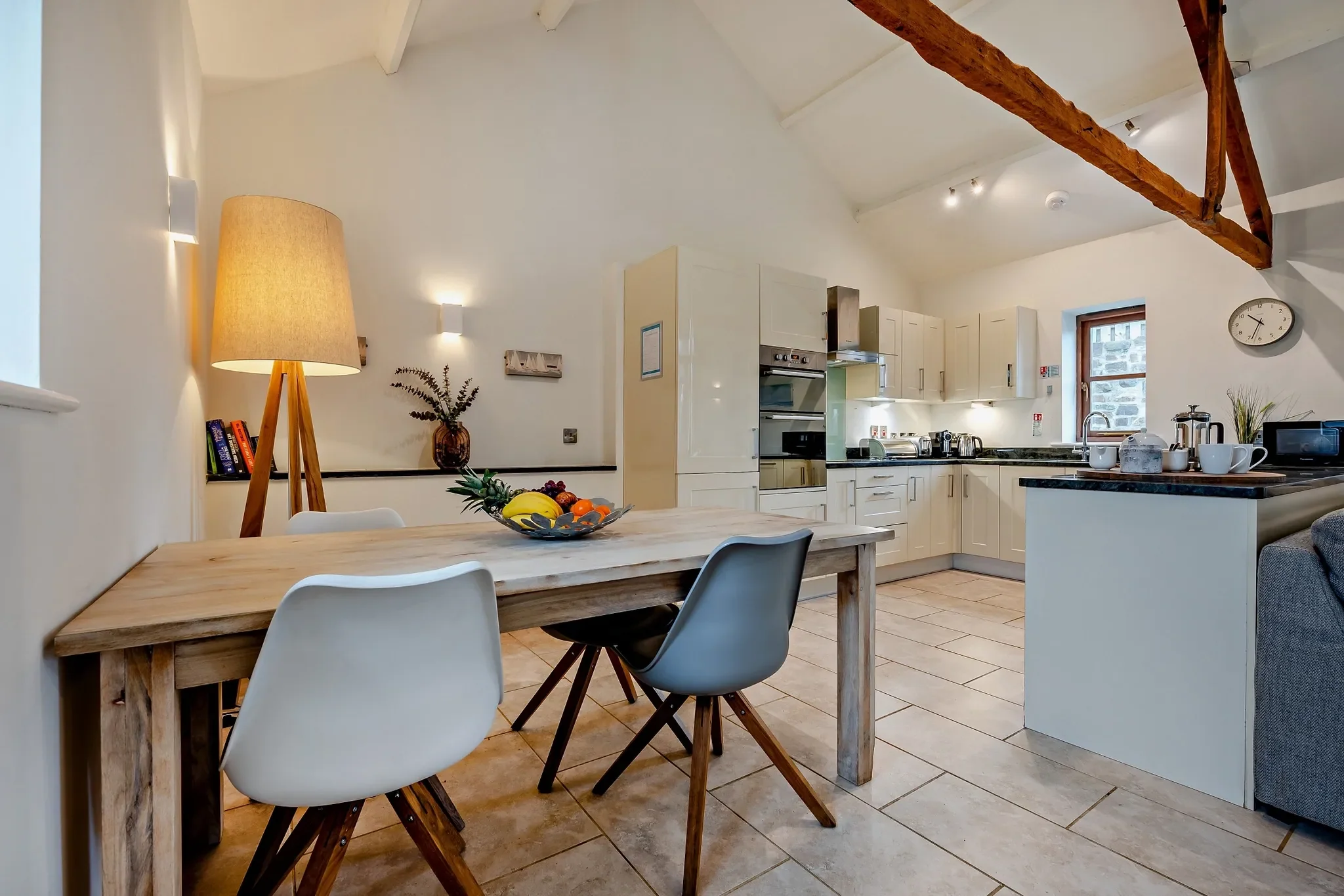 Long Down dining area with rustic wooden table and contemporary chairs set beneath vaulted beams, open to the kitchen behind.