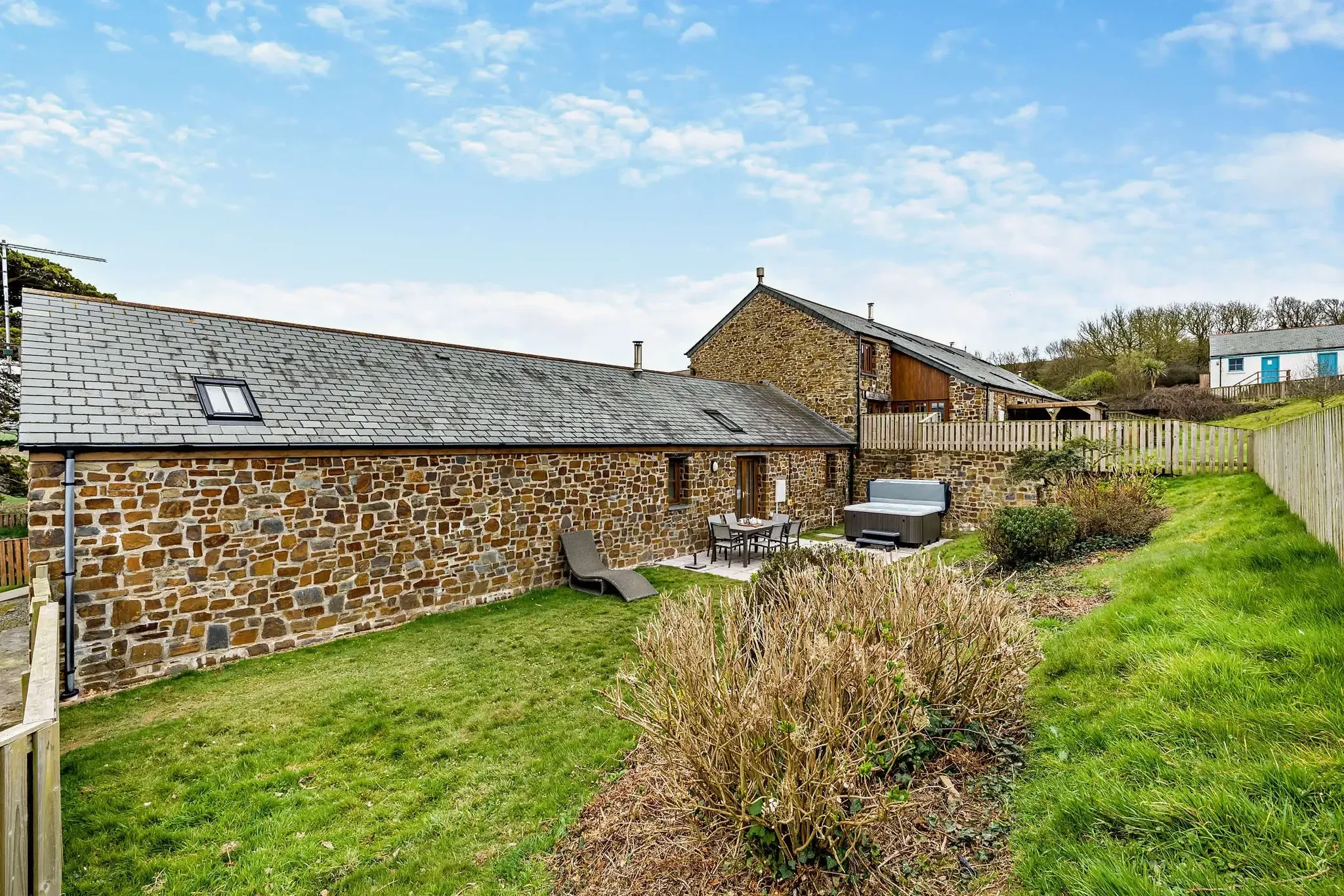 Long Down stone barn cottage seen from the garden, with slate skylights, rear terrace, hot tub and lawned grounds.