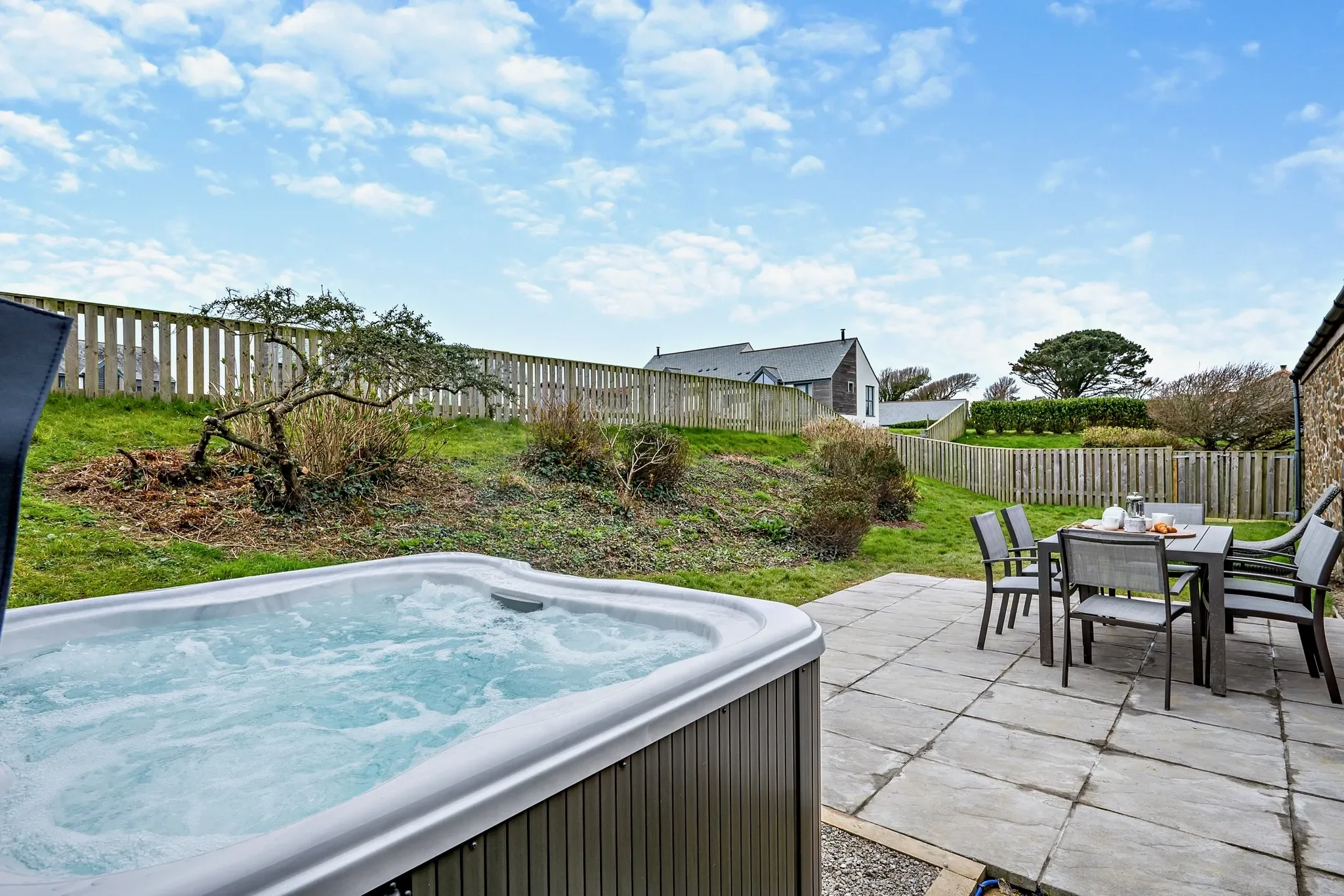 Long Down private terrace with bubbling hot tub in the foreground and outdoor dining table and chairs beyond.