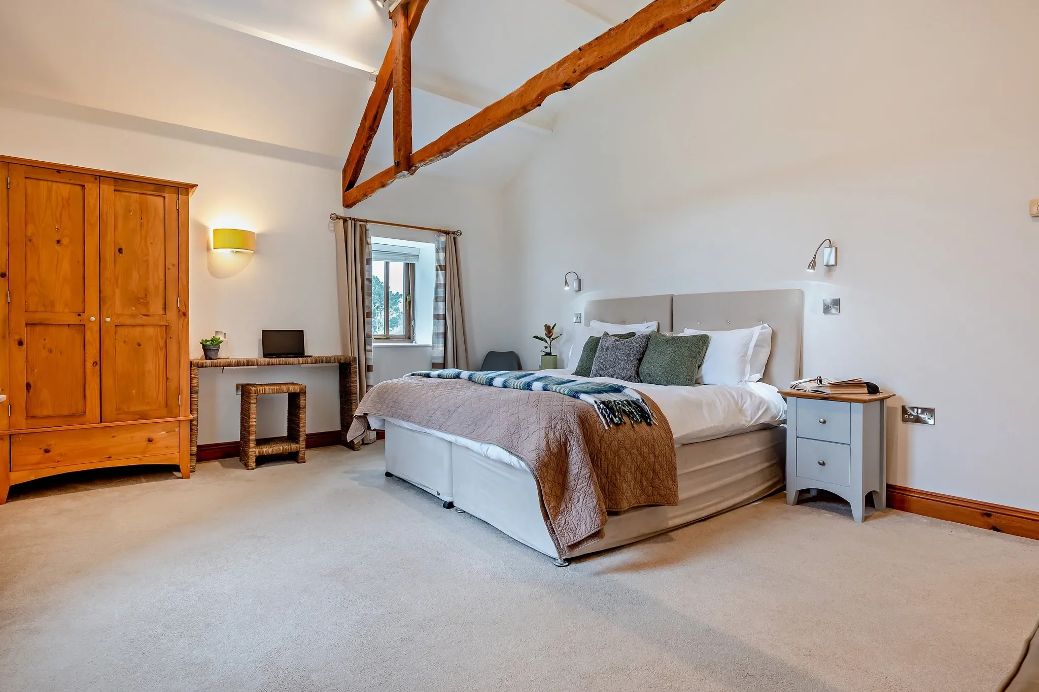 Long Down second king bedroom with vaulted beams, pine wardrobe, desk area and reading lamps on either side of the bed.