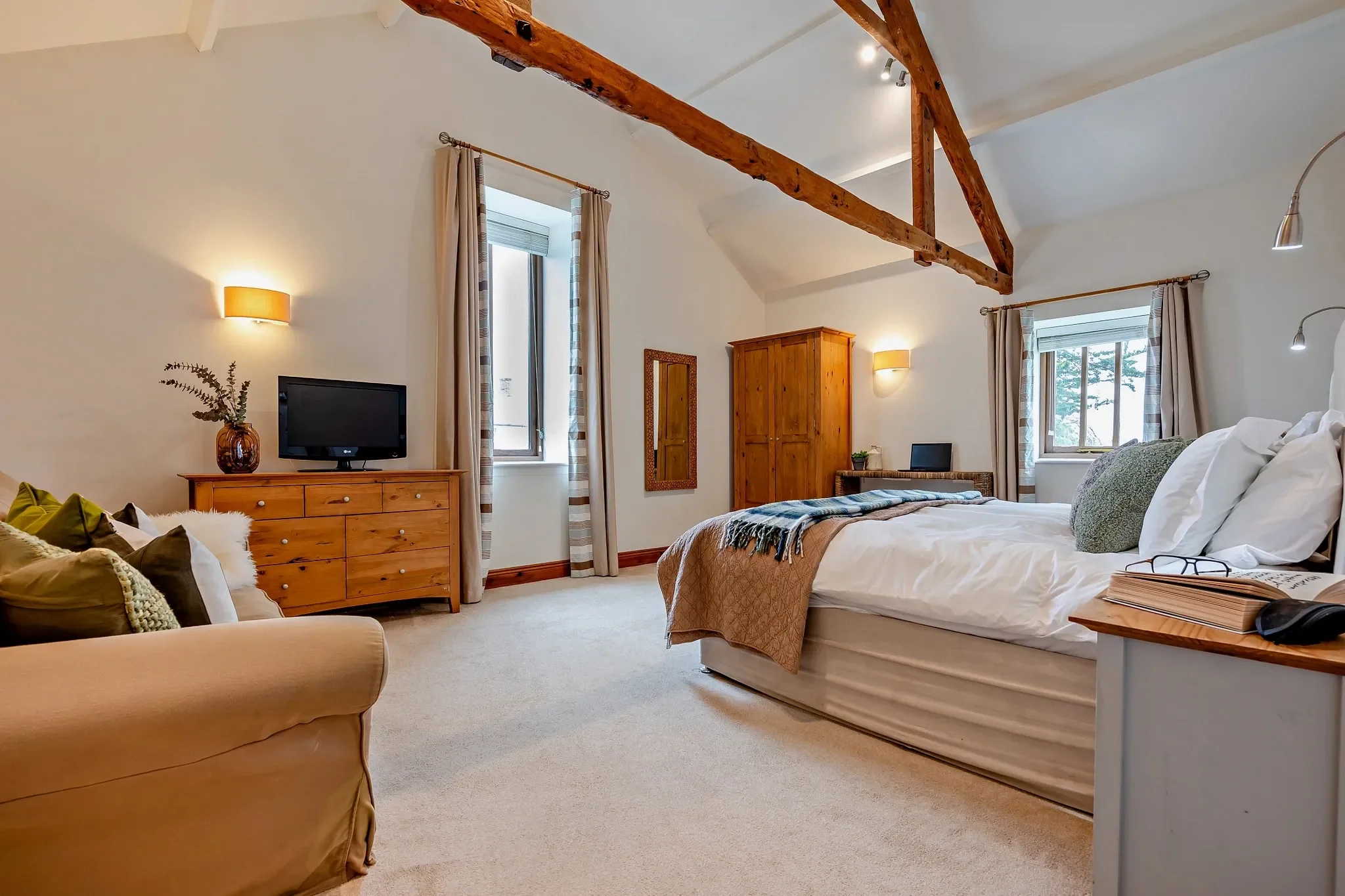 Long Down master bedroom wide view showing king bed, pine chest of drawers, TV, sofa and twin vaulted windows.
