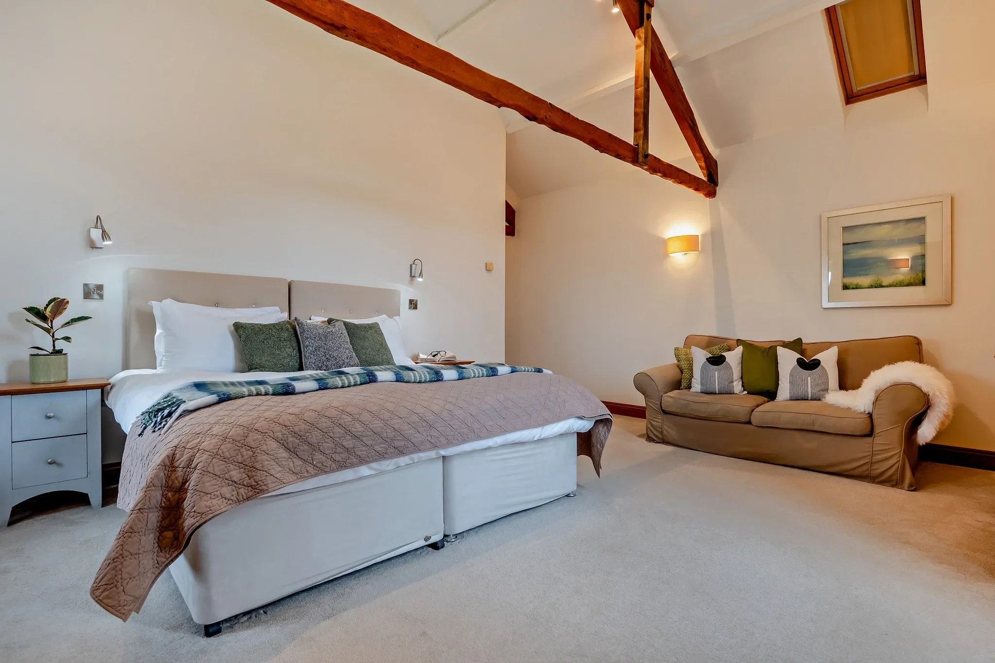Long Down master bedroom with king-size upholstered bed, exposed apex beams, seating sofa and landscape artwork.