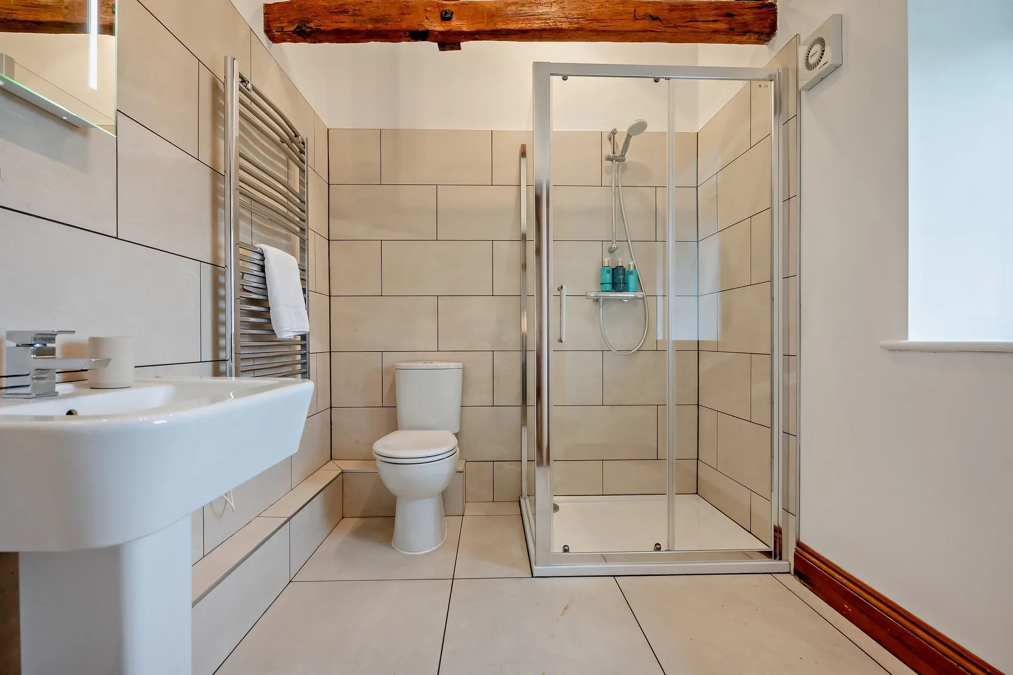 Long Down shower room with walk-in glazed cubicle, pedestal basin, heated towel rail and exposed ceiling beam.
