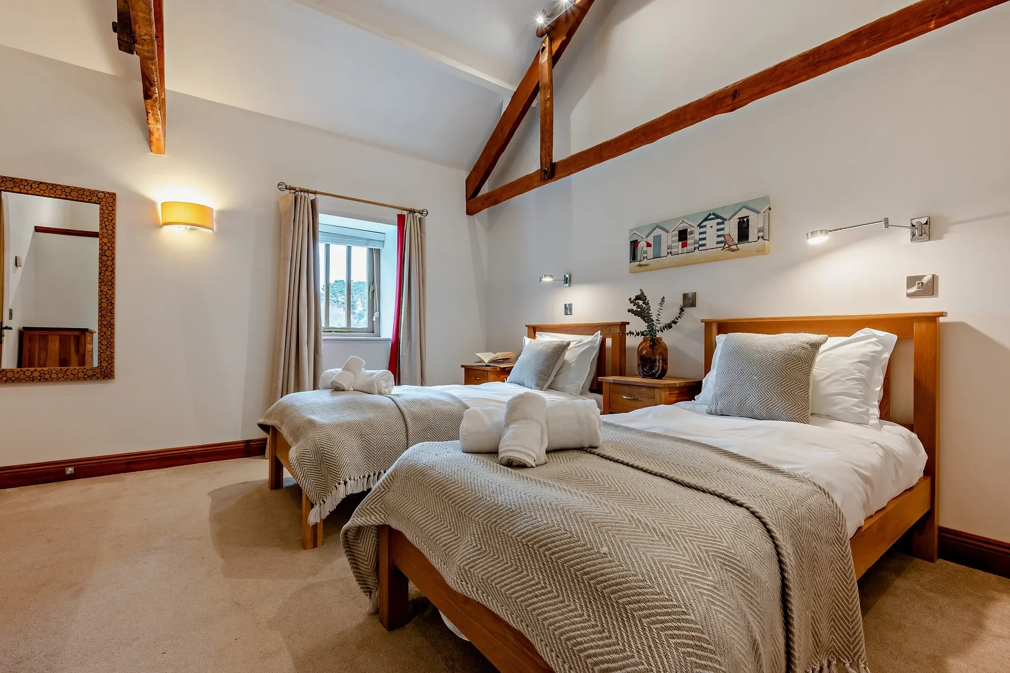 Long Down twin bedroom showing both beds with grey throws, ornate wall mirror and stone-framed window with red curtains.