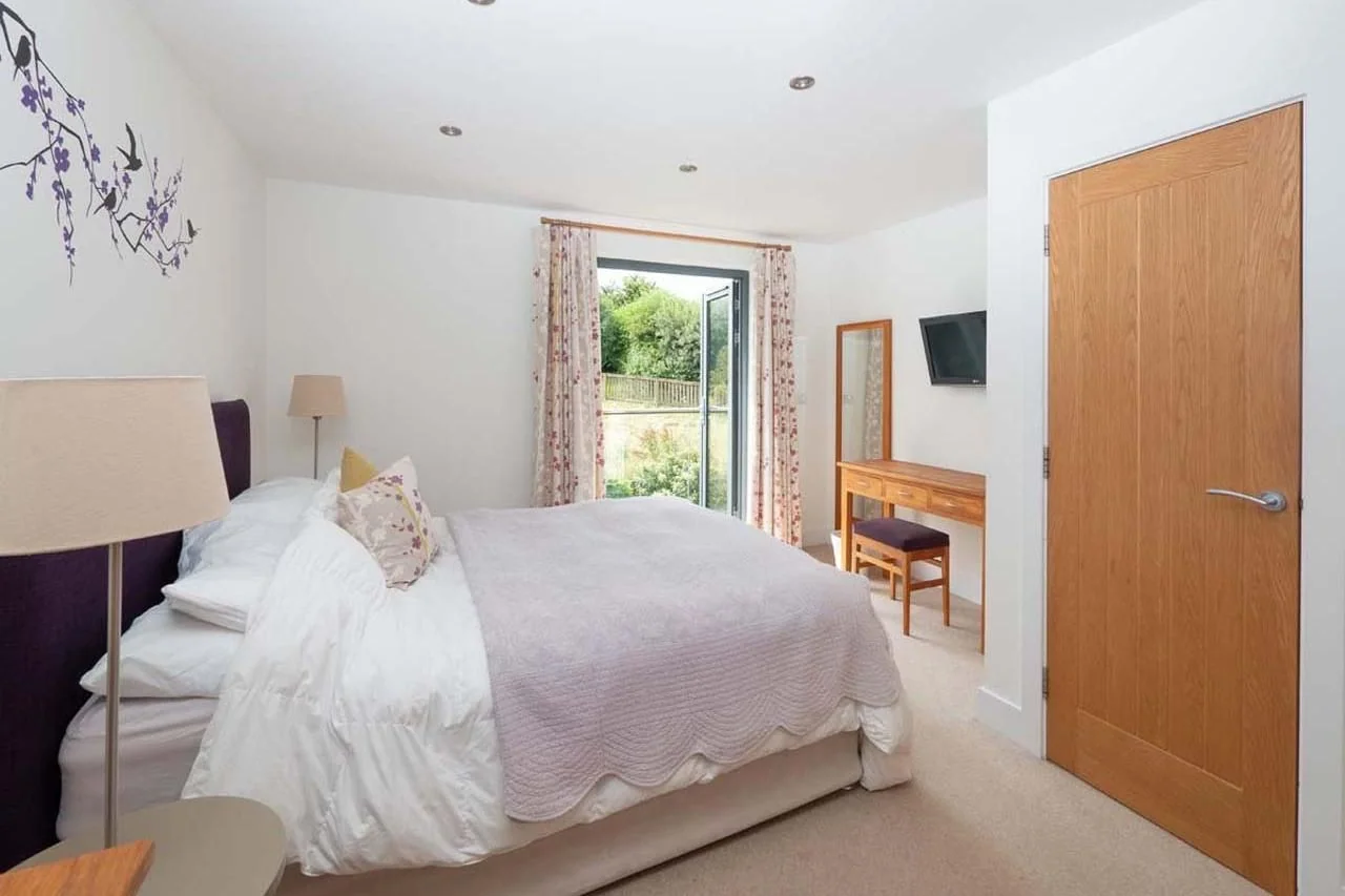 Medlands double bedroom with purple upholstered headboard, floral curtains, dressing table and French doors to the balcony.