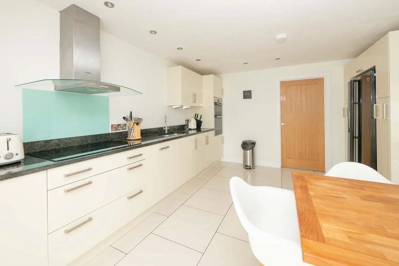 Medlands fully equipped kitchen with cream gloss units, granite worktops, aqua glass splashback and extractor over the hob.