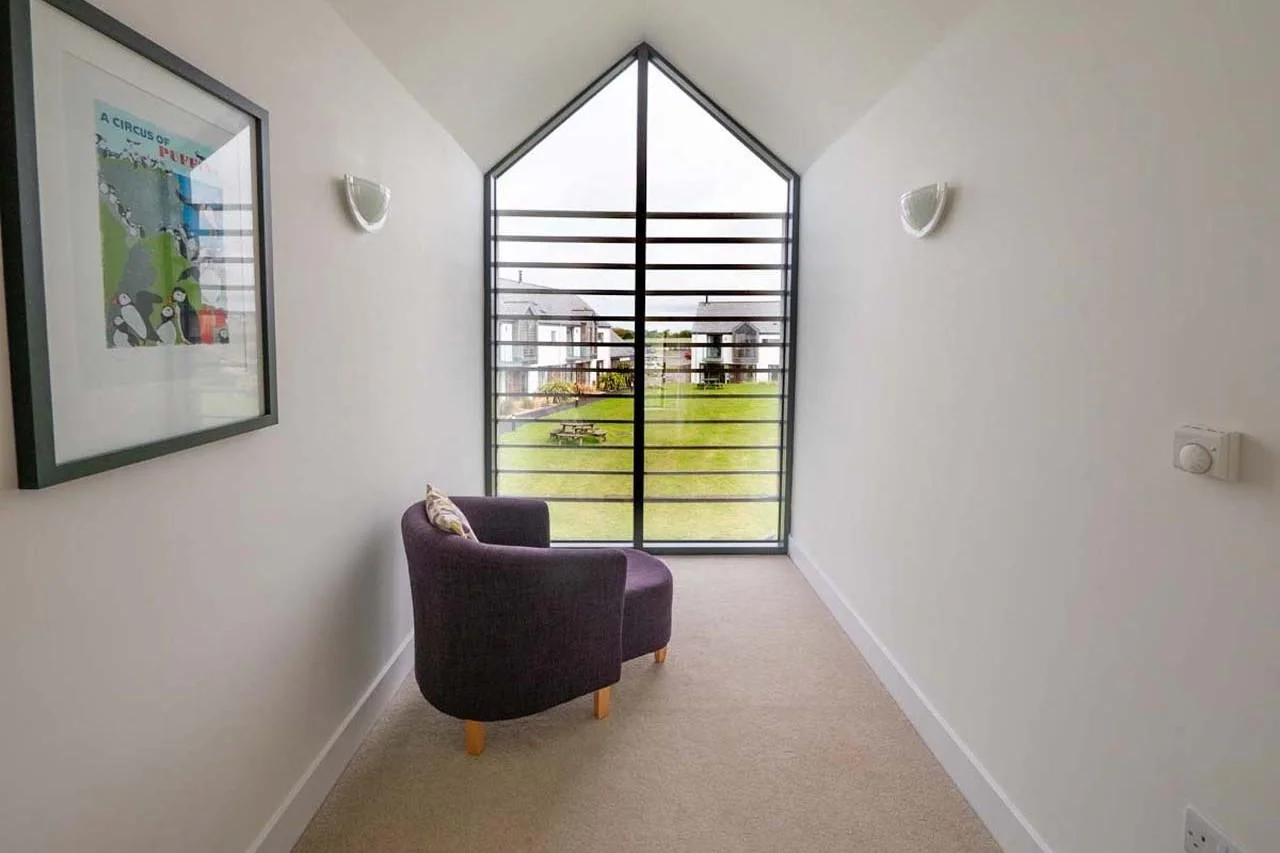 Medlands upper-floor landing reading nook with armchair beneath a tall pitched glazed window overlooking the estate grounds.