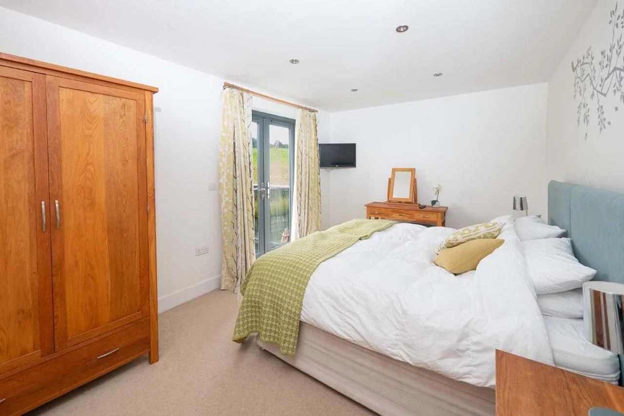 Medlands master bedroom from the wardrobe side showing the large oak wardrobe, wall-mounted TV and balcony doors with countryside views.
