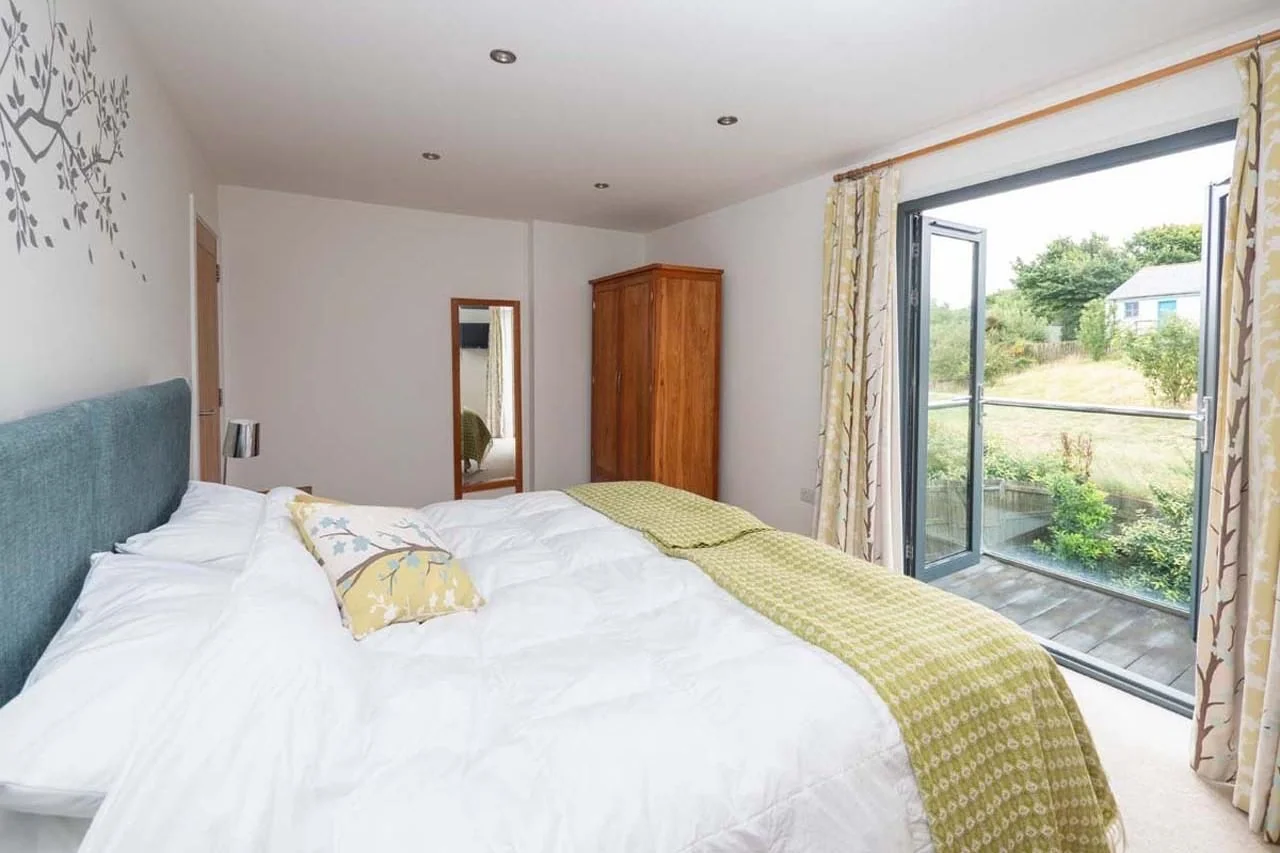 Medlands master bedroom with super-king bed, teal headboard, tree-motif wall art and bi-fold doors opening to a private balcony.