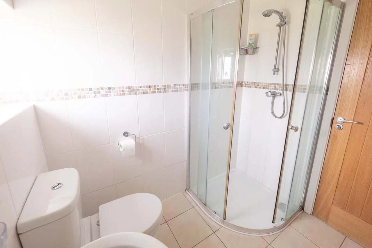 Medlands shower room with quadrant glass enclosure, white tiled walls with mosaic border strip and WC.
