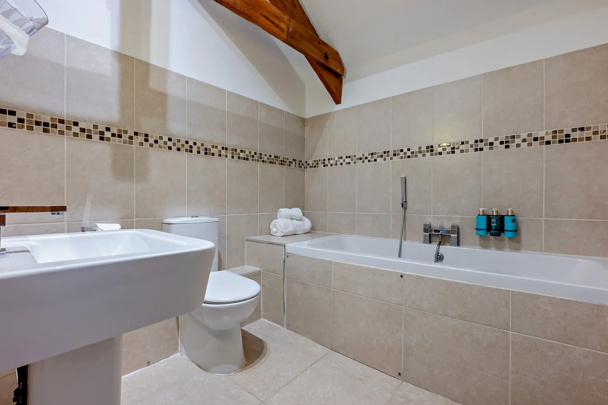 Middle Hill family bathroom with a full-size bath, mosaic border tiling, WC, and pedestal basin beneath vaulted oak beams.